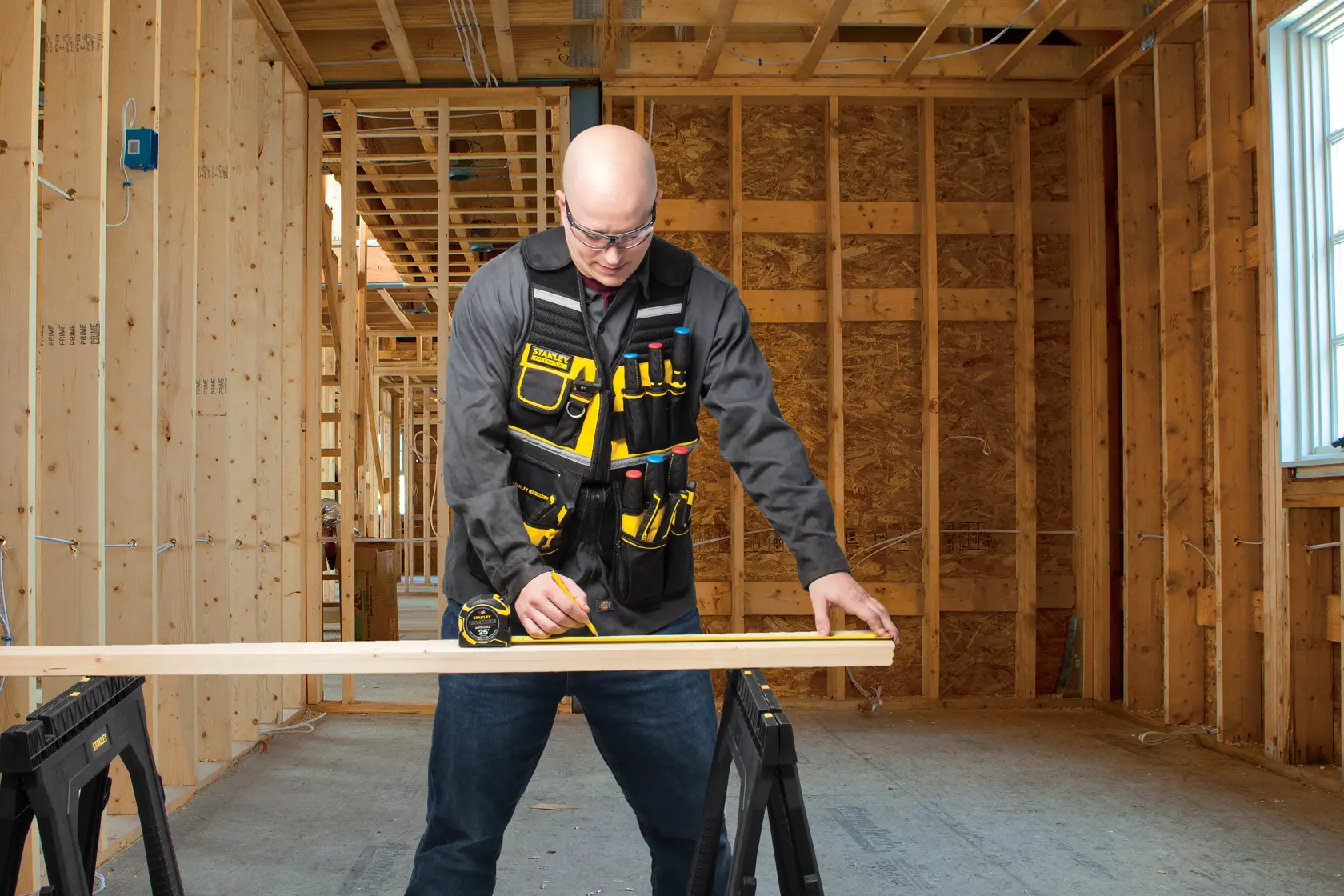 STANLEY FMST1-71181 tool vest with multiple yellow and black pockets, worn by a person working in a wood construction site.