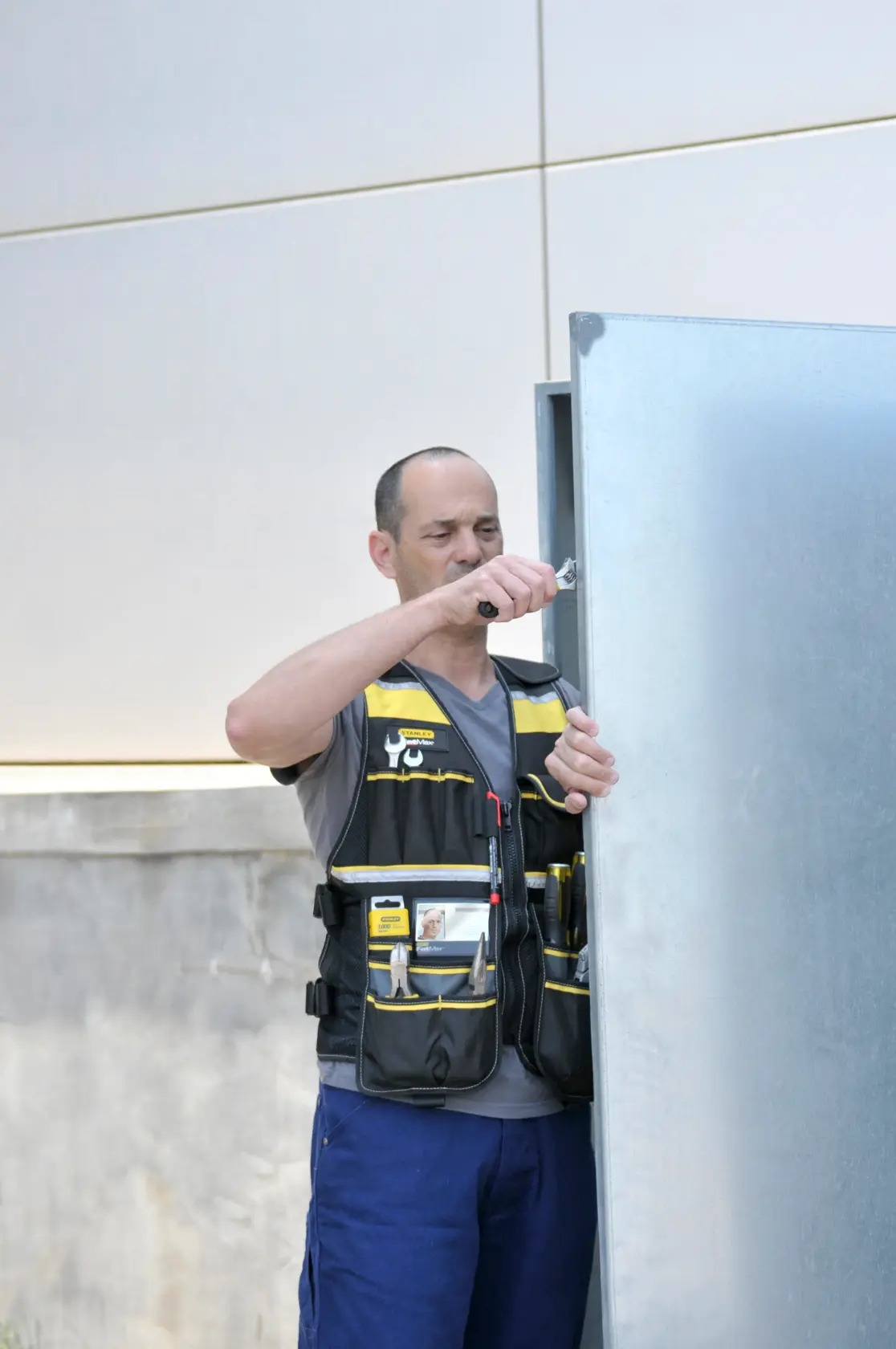 Photo of person wearing STANLEY FMST1-71181 tool vest with multiple pockets, working outdoors by a metal cabinet.