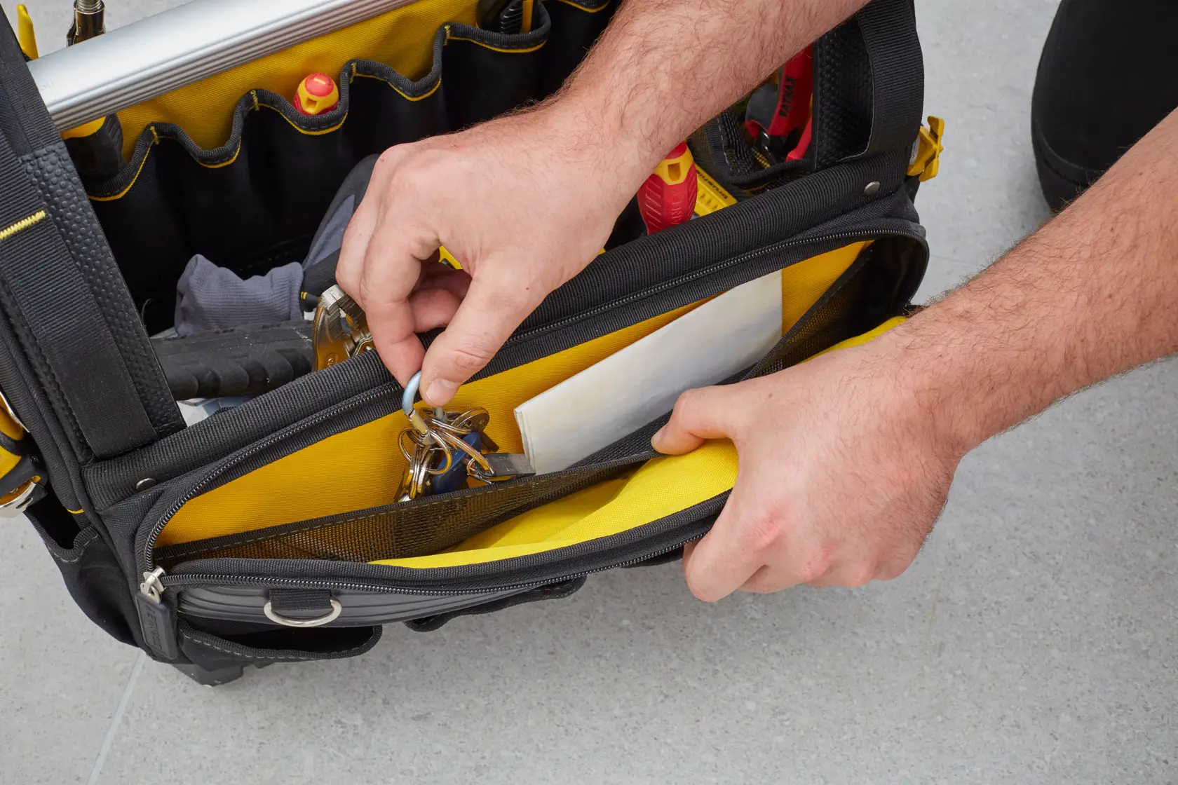 STANLEY FMST83296-1 tool bag top view with hands organizing keys and documents in yellow interior pocket.