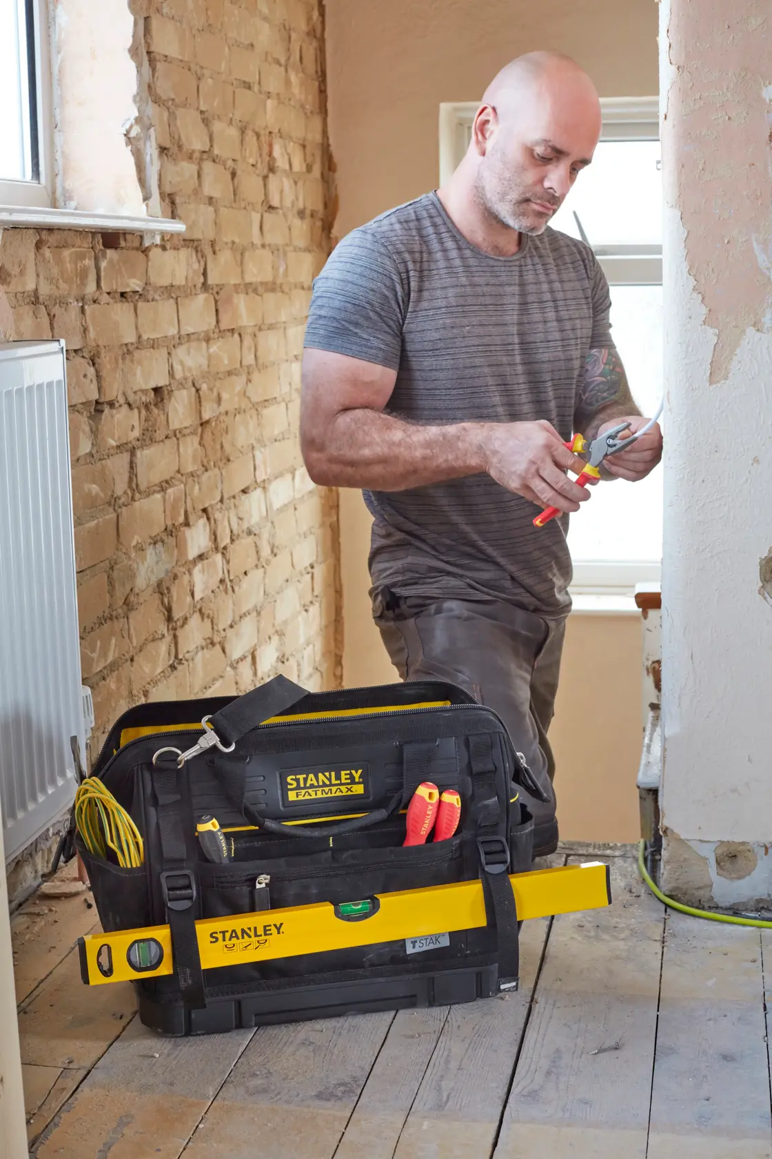 STANLEY FMST83297-1 tool bag on the floor with hand tools and level, worker in the background renovating room.