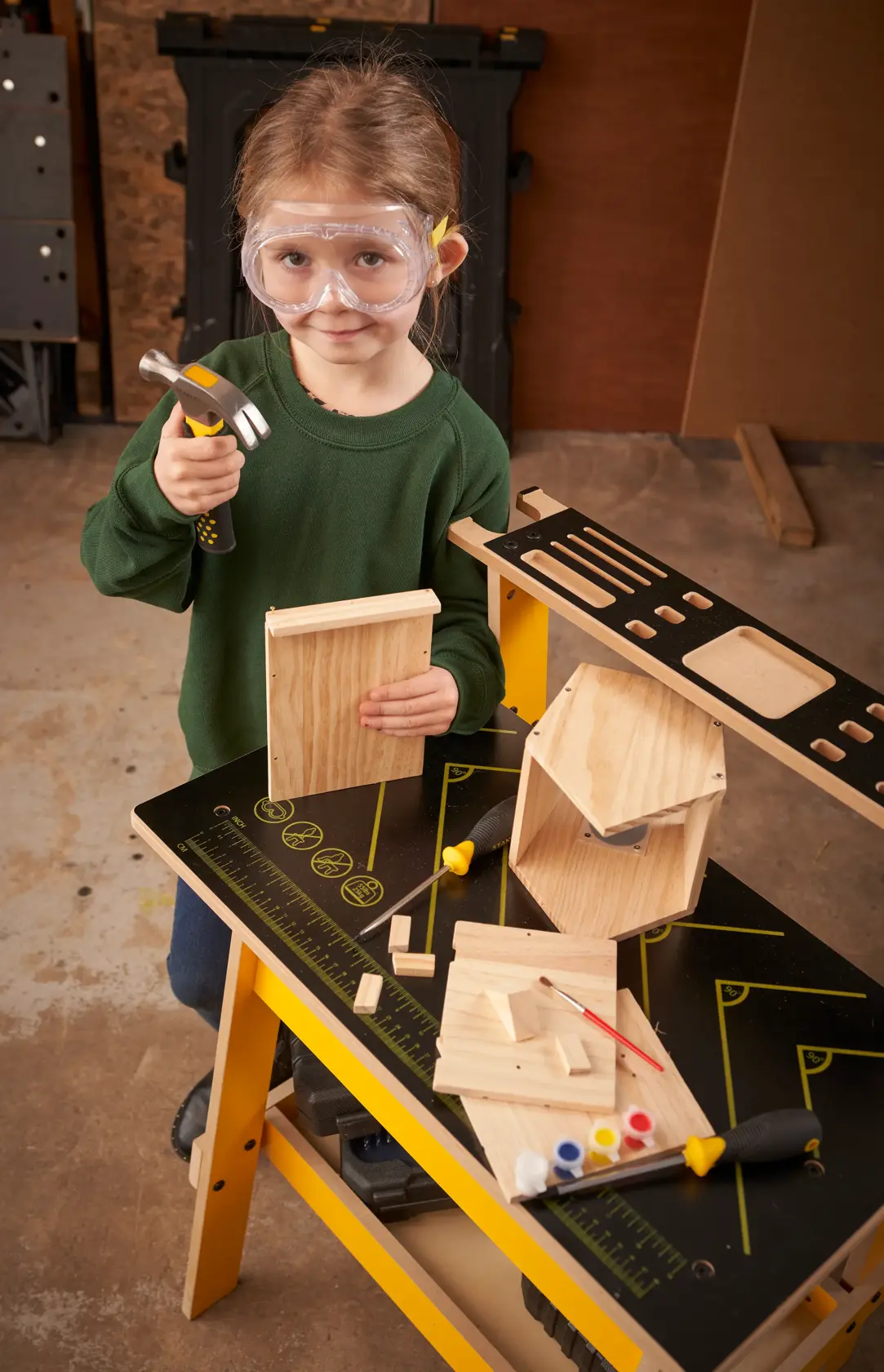 STANLEY K020-SY photography of child using hammer at yellow workbench with wooden birdhouse kit and paint.