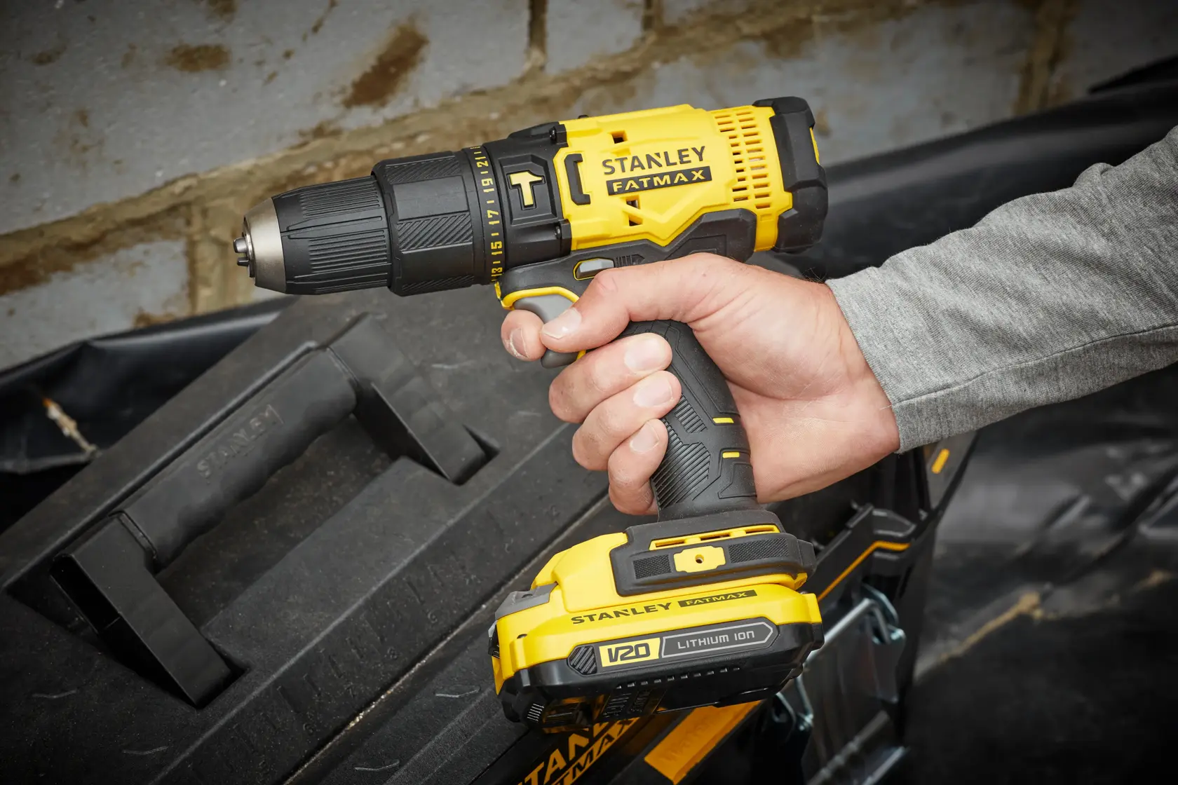 STANLEY SFMCD711D21 cordless drill, yellow and black, held in hand, side angle, tool box in background.