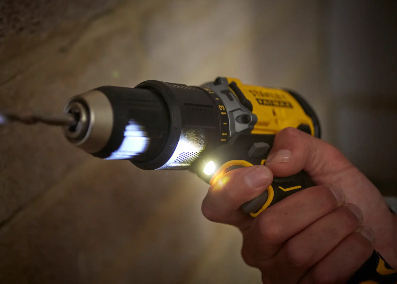 STANLEY SFMCD715M12 cordless drill in use, close-up of hand gripping tool with LED light on.