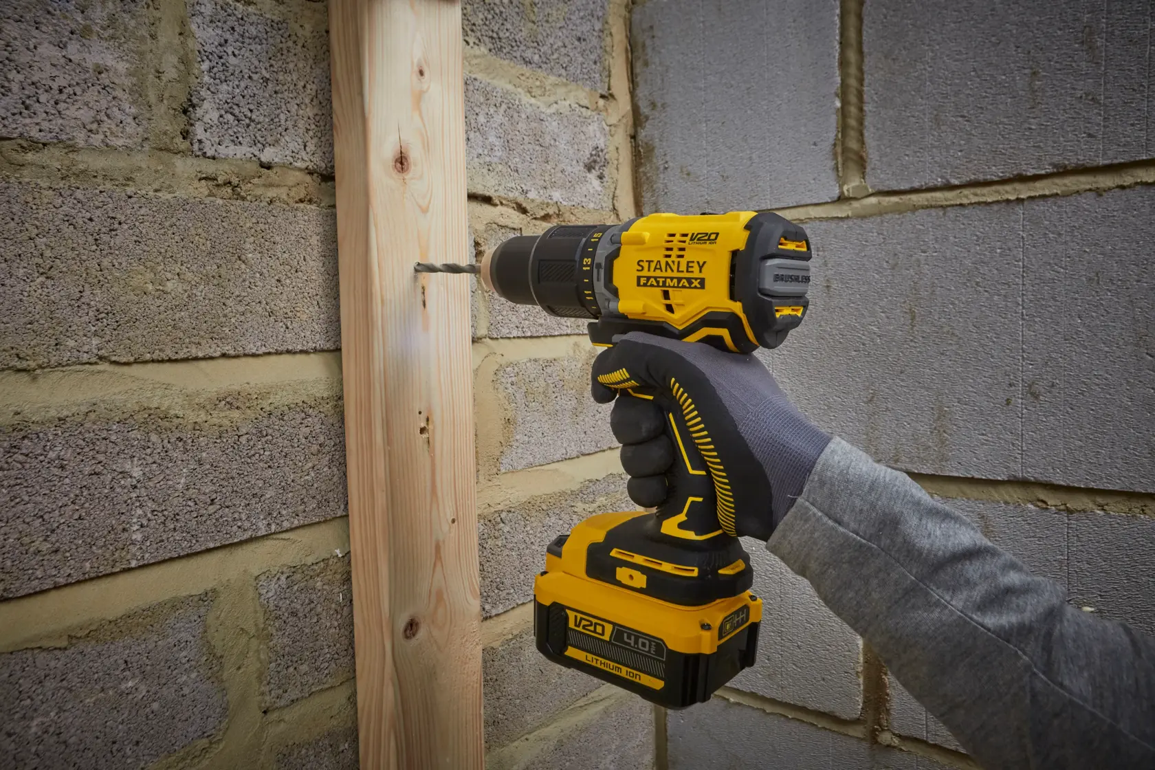 Stanley SFMCD715M12 cordless drill being used to drill wood against a brick wall, close-up view.