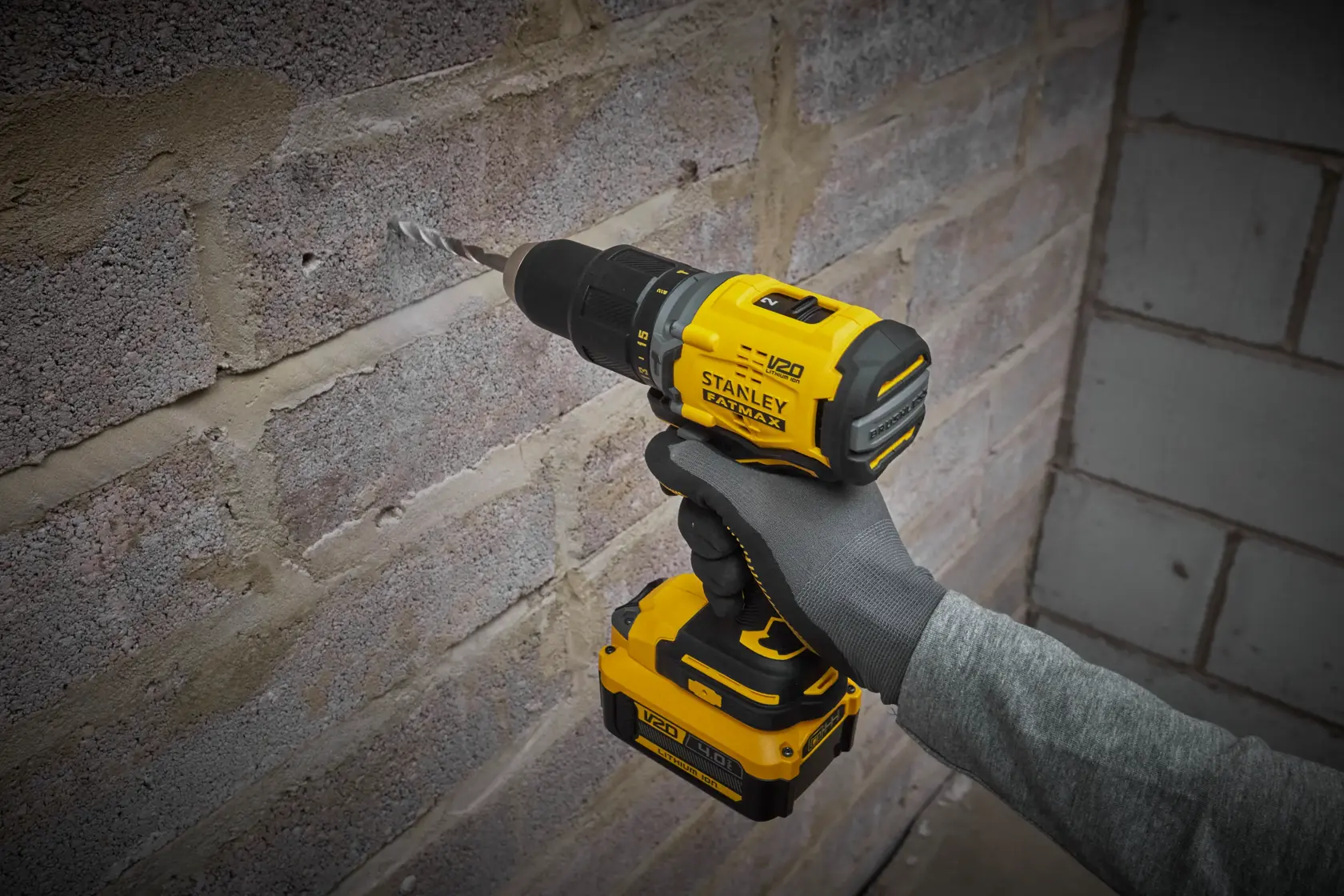 Stanley SFMCD715M12 cordless drill in use on brick wall, yellow and black design, close-up view.