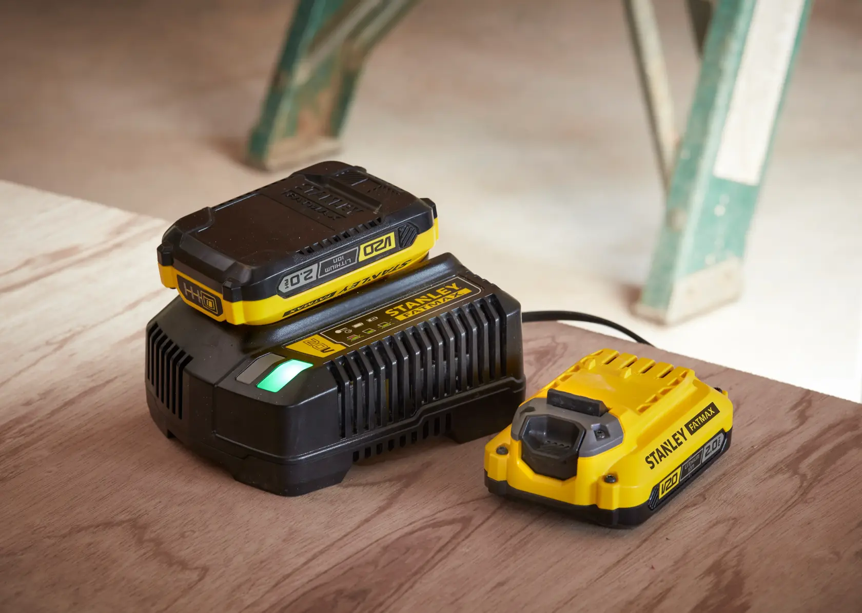 STANLEY SFMCD715M12 battery charger and battery, yellow and black, on wooden surface, side angle.
