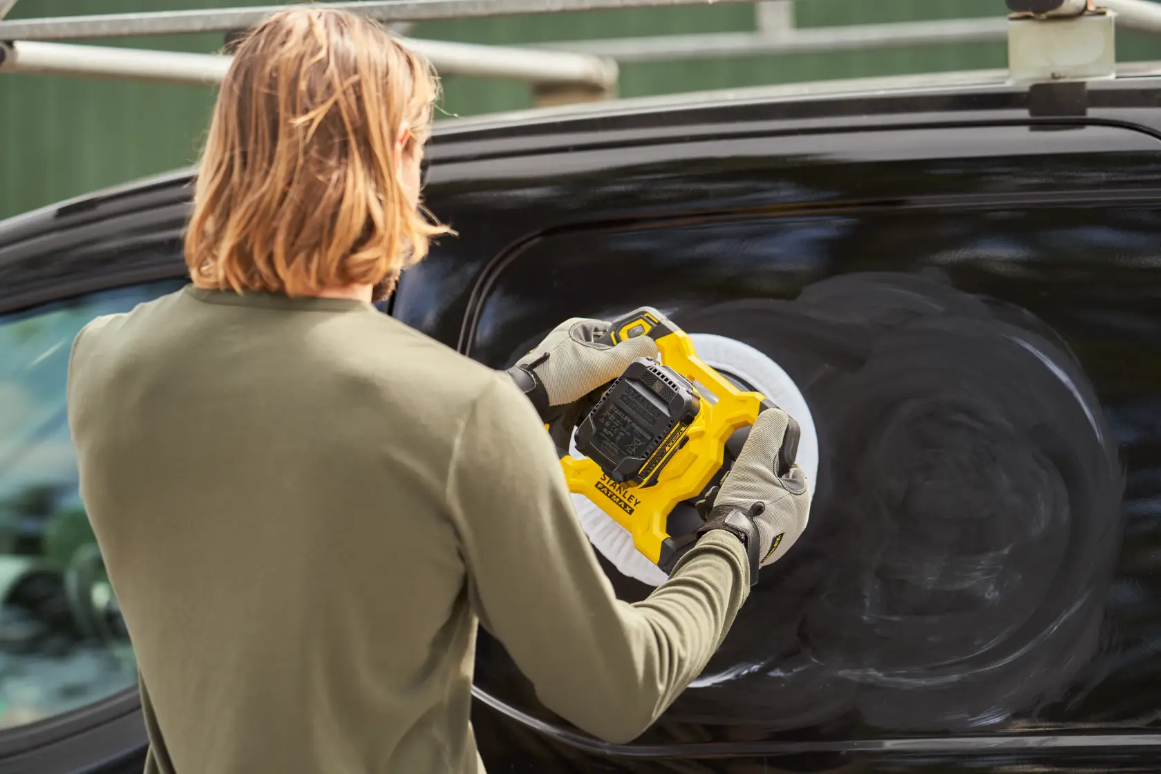 Photo of STANLEY SFMCE100D2 polisher being used on a black vehicle surface outdoors.