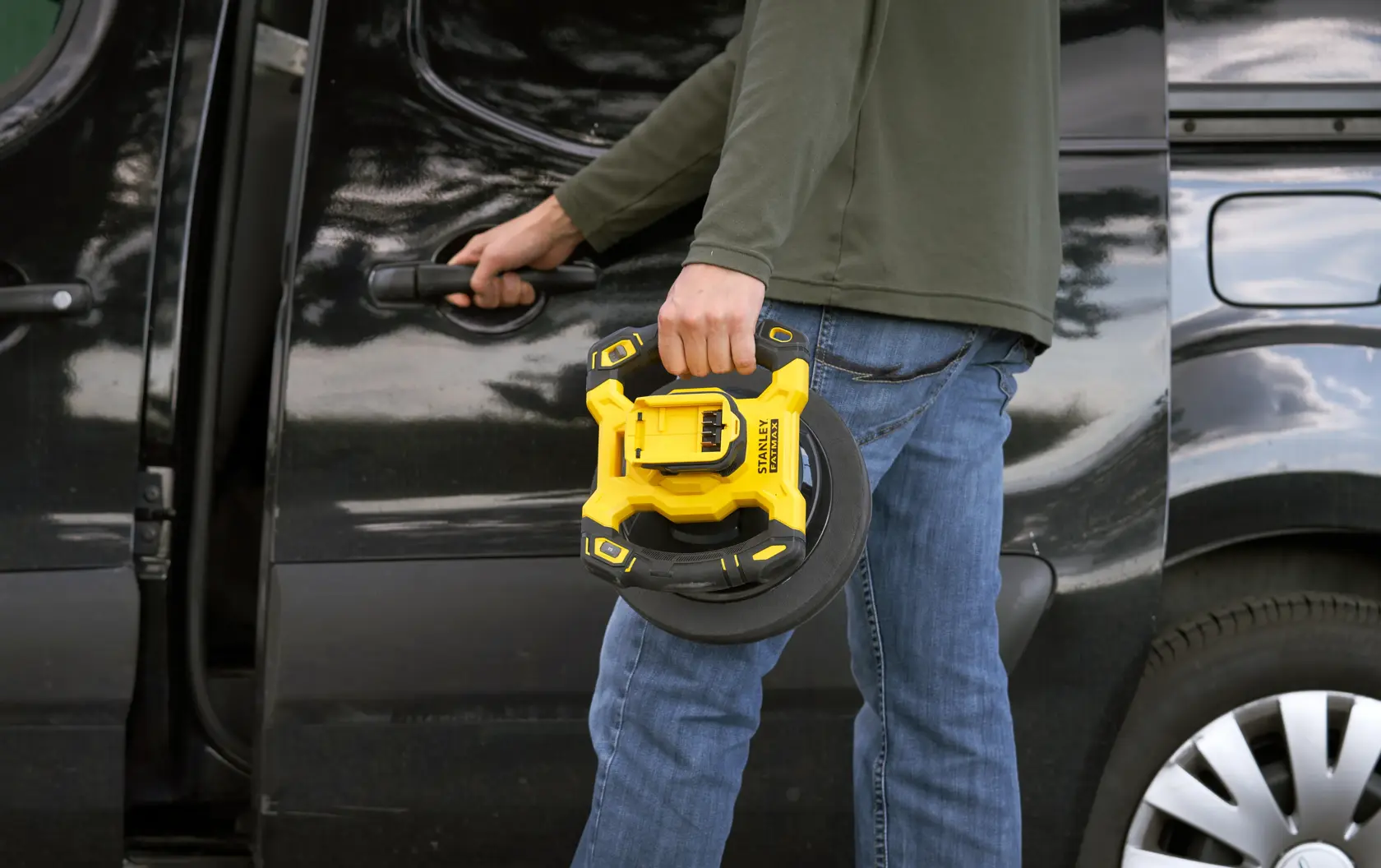 STANLEY SFMCE100D2 portable inflator held by person in front of black vehicle, outdoor setting.
