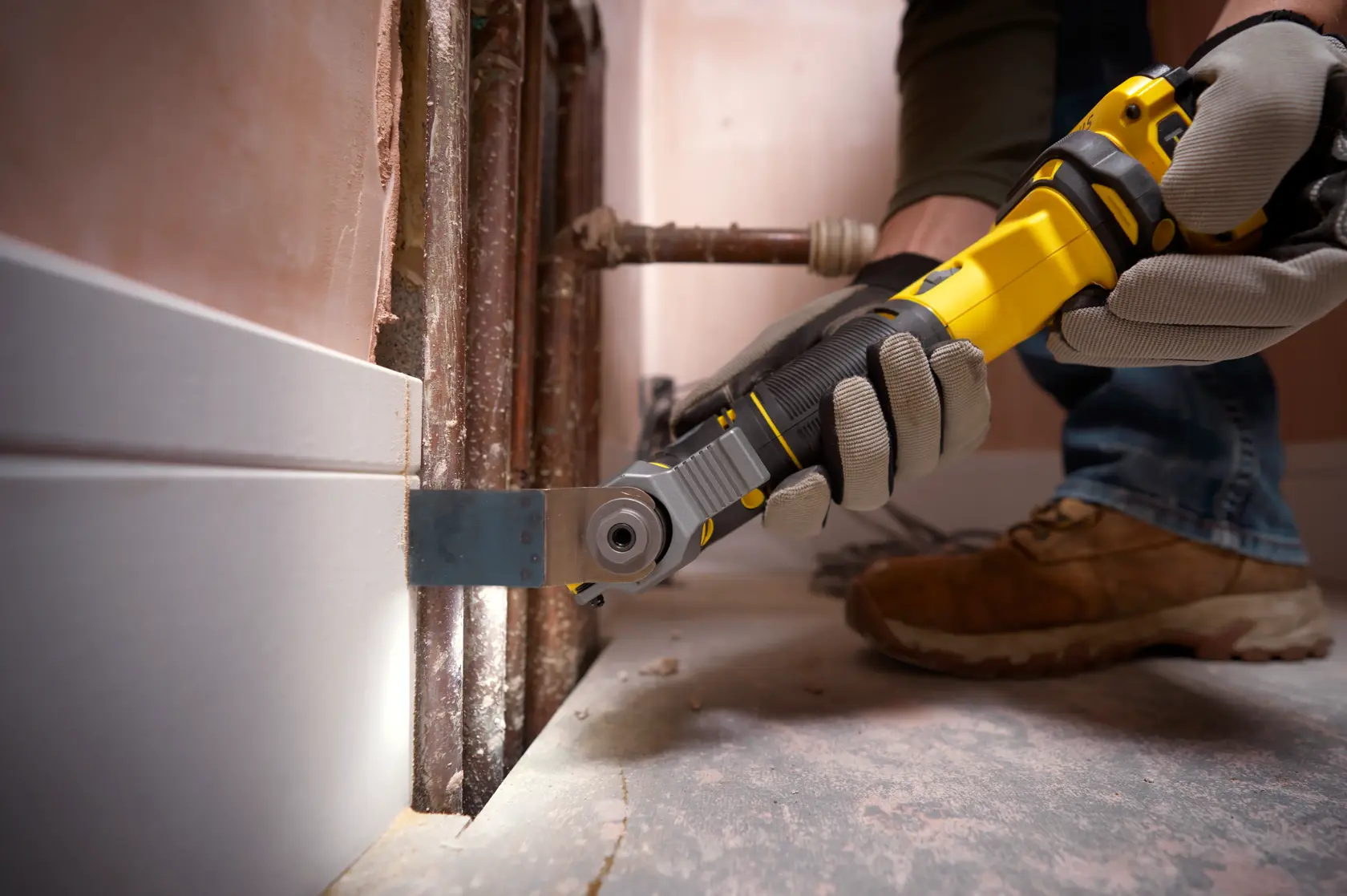STANLEY SFMCE500D1K multi-tool used to cut baseboard near pipes, close-up view.