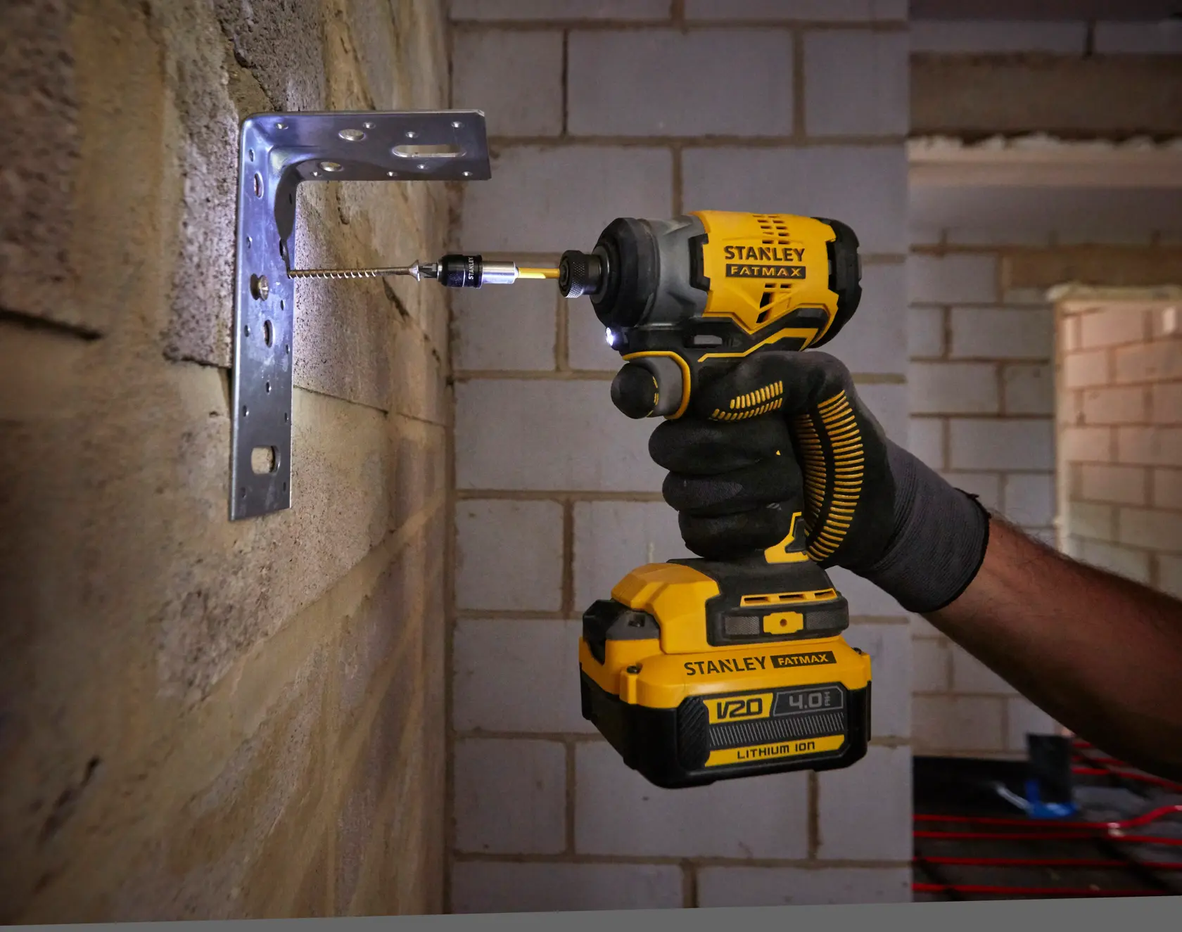 Stanley SFMCF810M1K impact driver drilling screw into metal bracket on brick wall, close-up view.