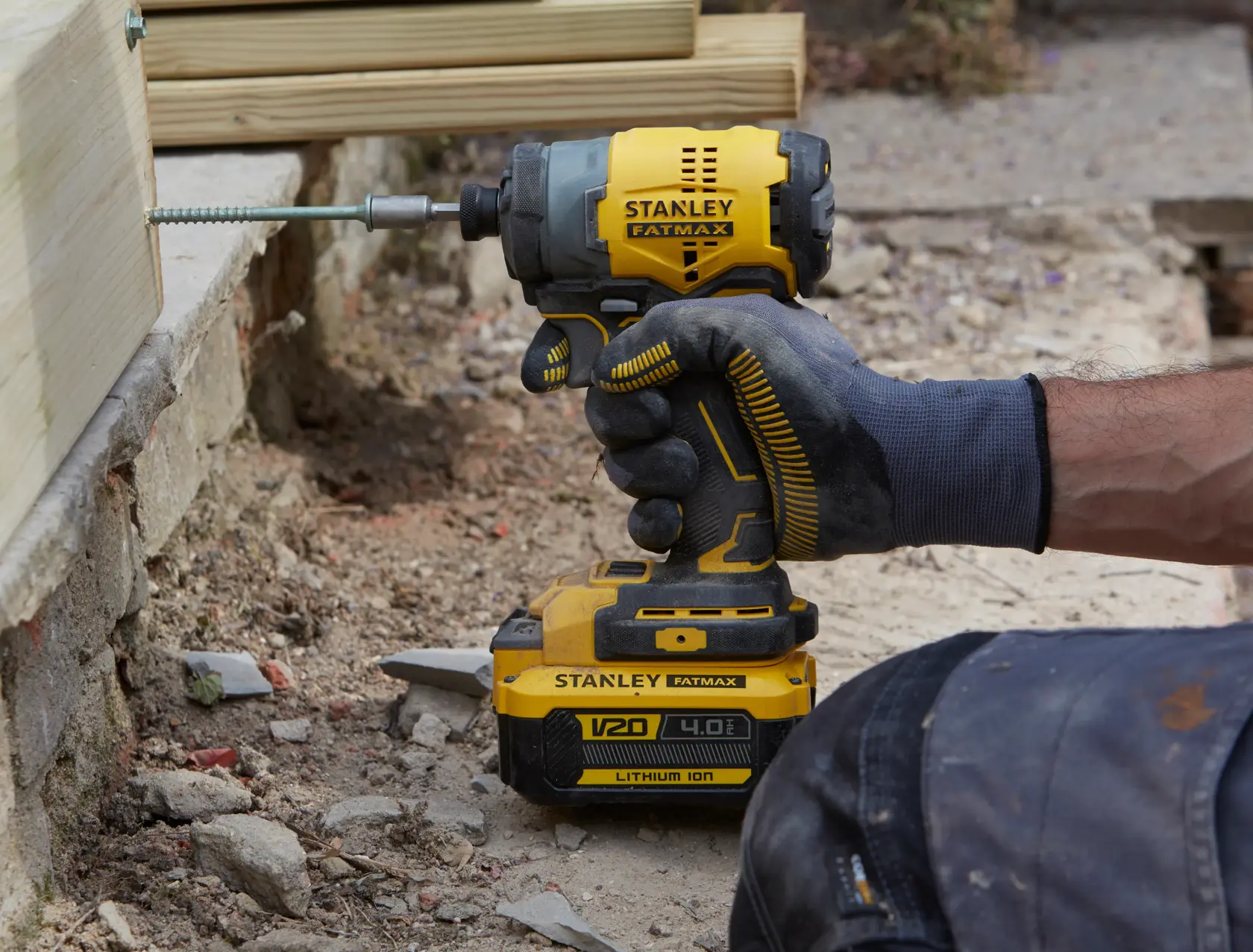 STANLEY SFMCF810M1K impact driver in use outdoors driving screw into wooden beam, construction setting.
