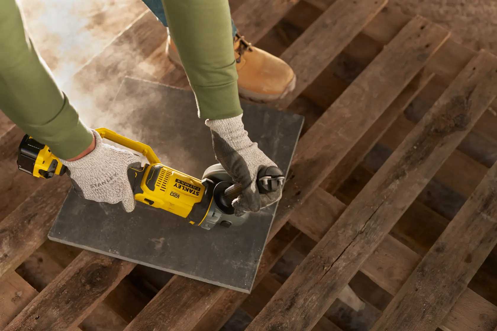 STANLEY SFMCG400M1K cordless angle grinder in use cutting tile, worker wearing gloves and safety boots.