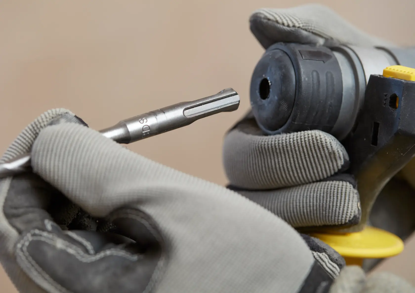 Photo of a gloved hand inserting a drill bit into a STANLEY SFMCH900M12 rotary hammer, close-up view.
