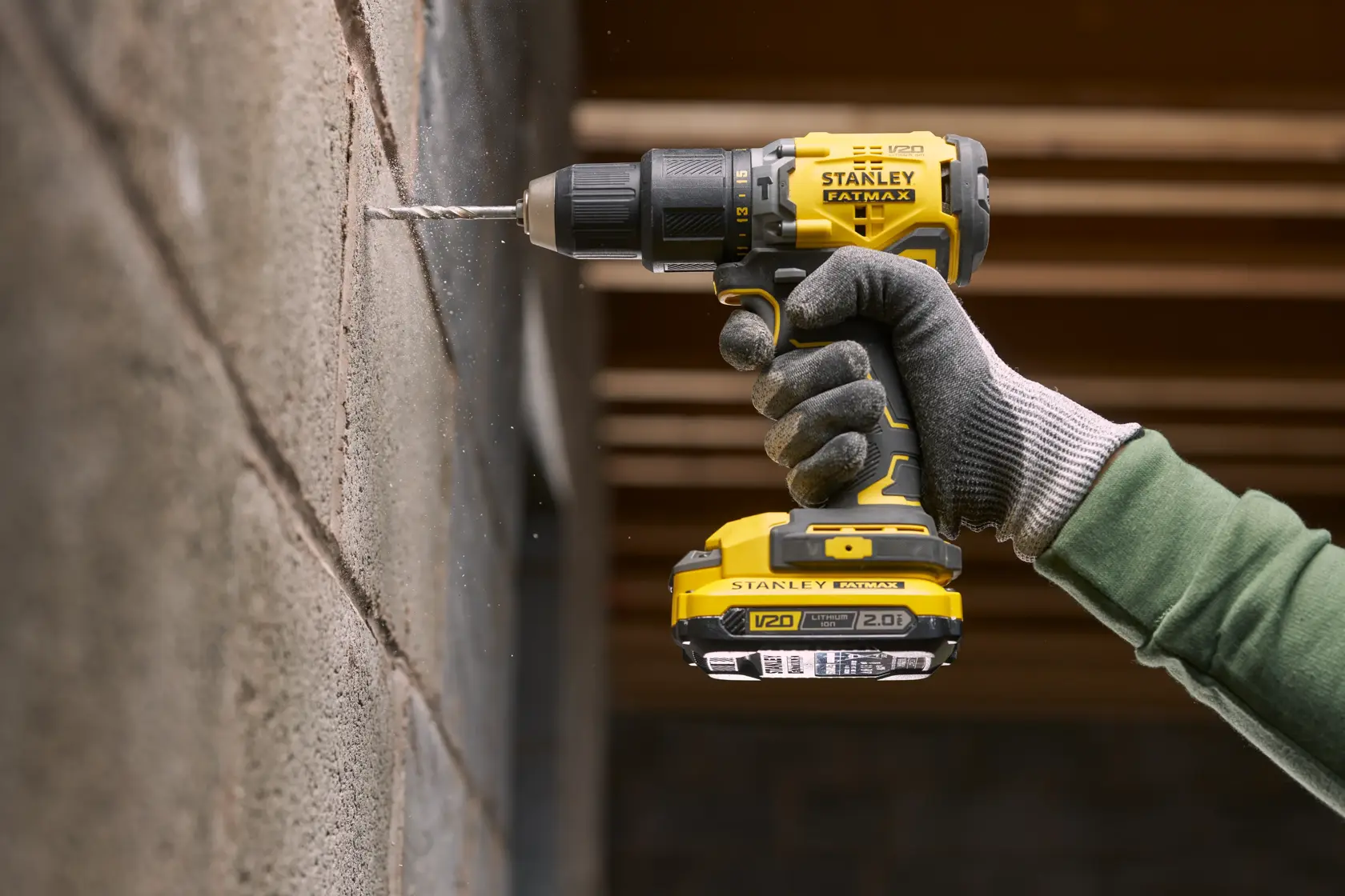 Photo of STANLEY SFMCK461D2S cordless drill in use drilling into a concrete wall, close-up of tool and gloved hand.