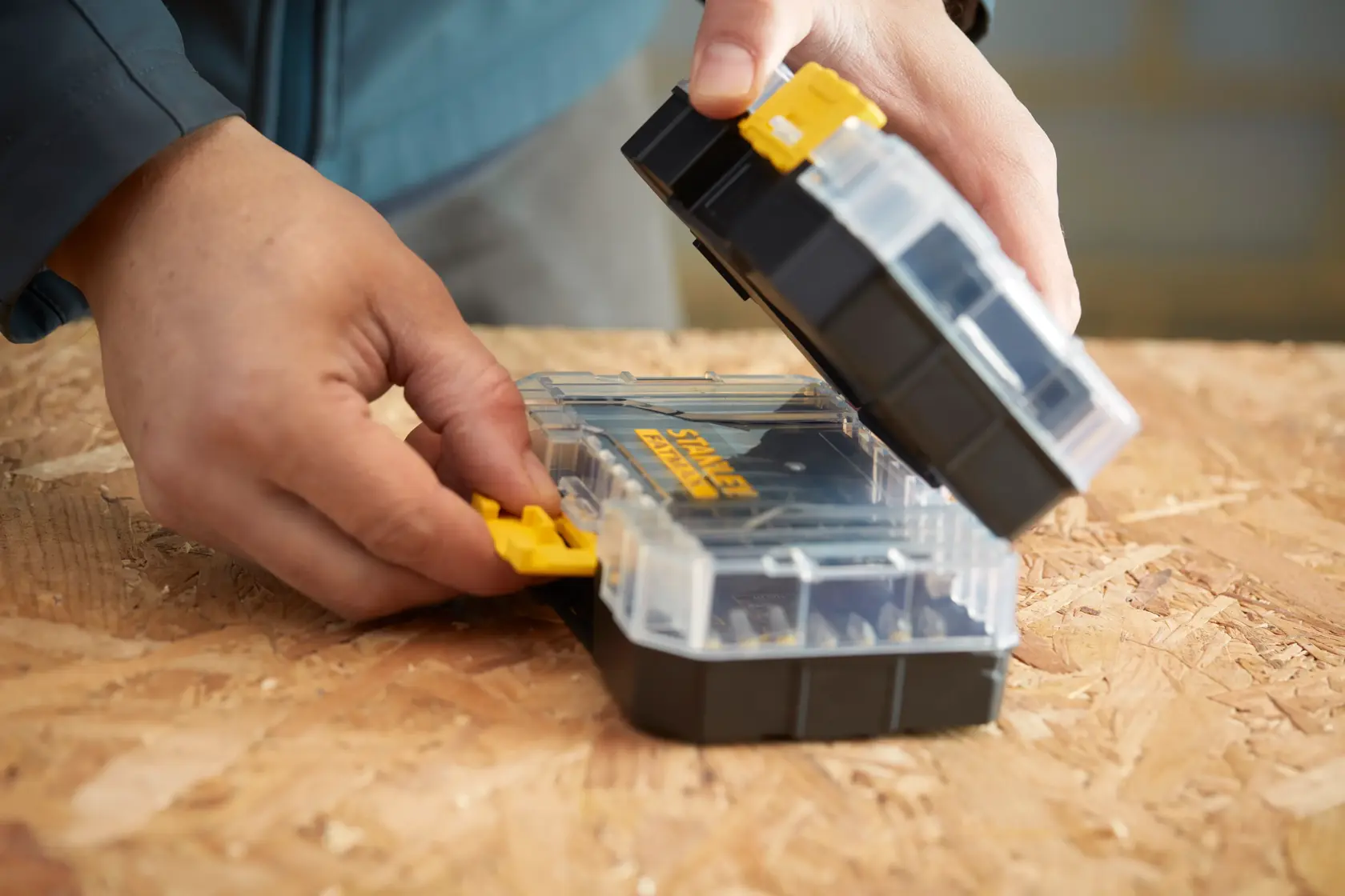 Photo of STANLEY STA88560 small parts organizer with clear lid, yellow latch, and black base being opened on a wooden surface.