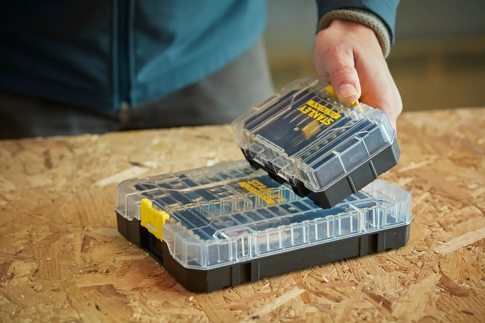 STANLEY STA88560 organizer box with clear lid, yellow latch, shown on wood surface held by hand.