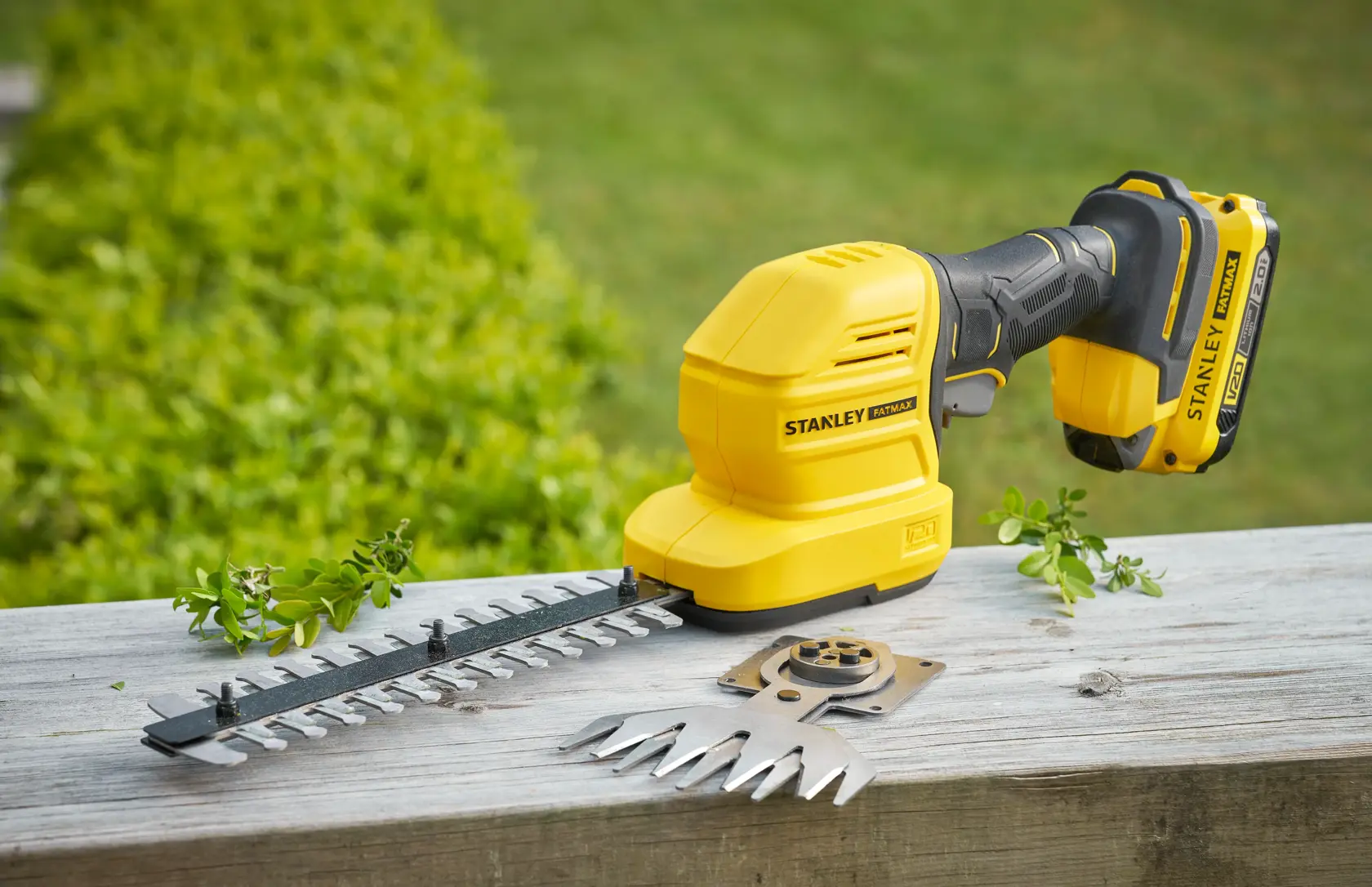 Photo of STANLEY STCSS20B cordless shrub and grass shear with blade attachments on a wooden surface.