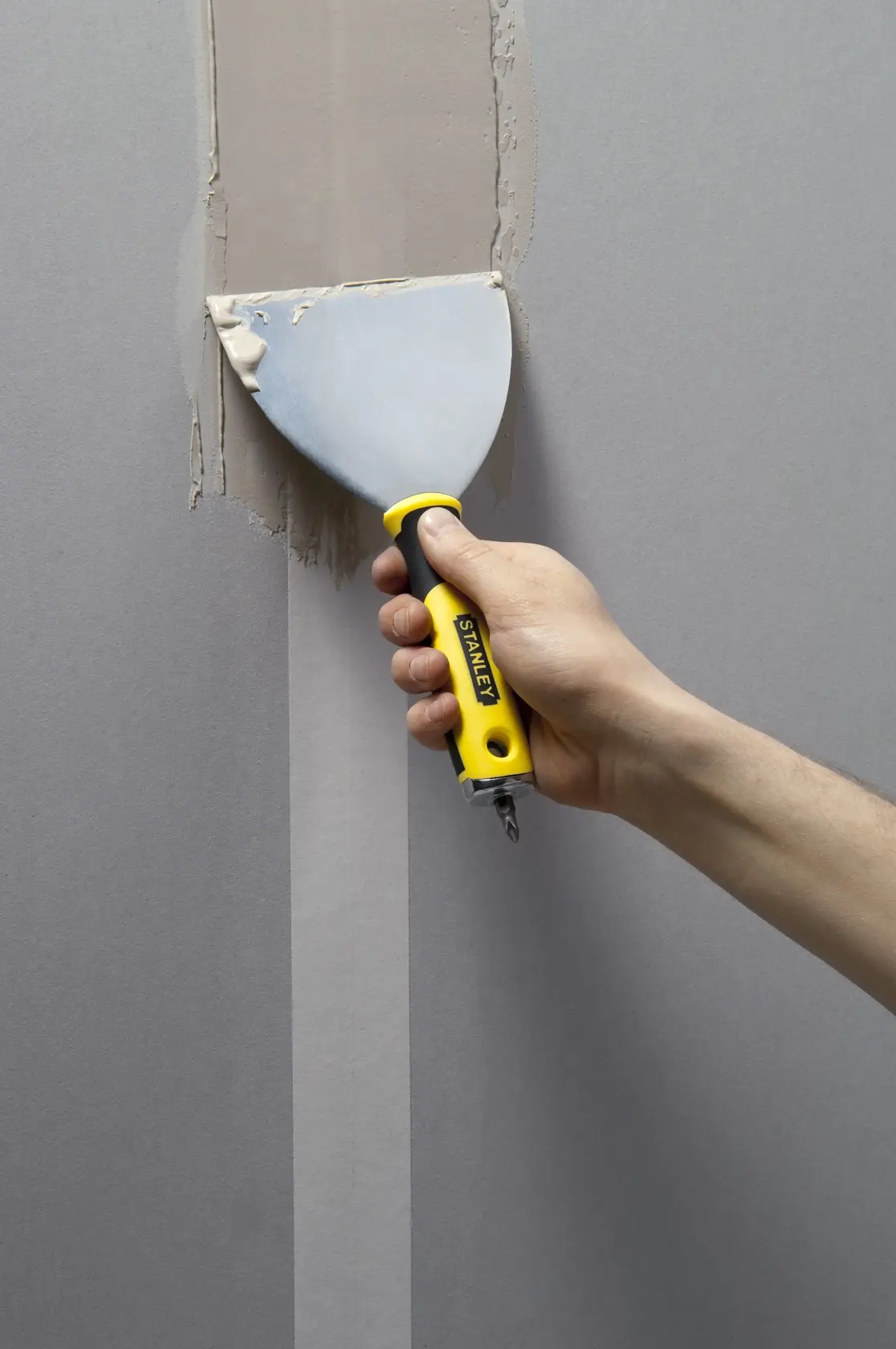 STANLEY STHT0-28034 putty knife with yellow and black handle used to apply filler on a wall.