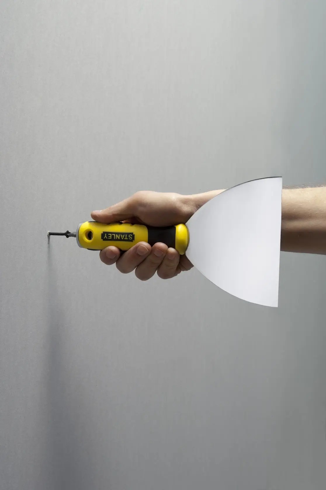 STANLEY STHT0-28034 putty knife with yellow and black handle, side view held by hand against a wall.