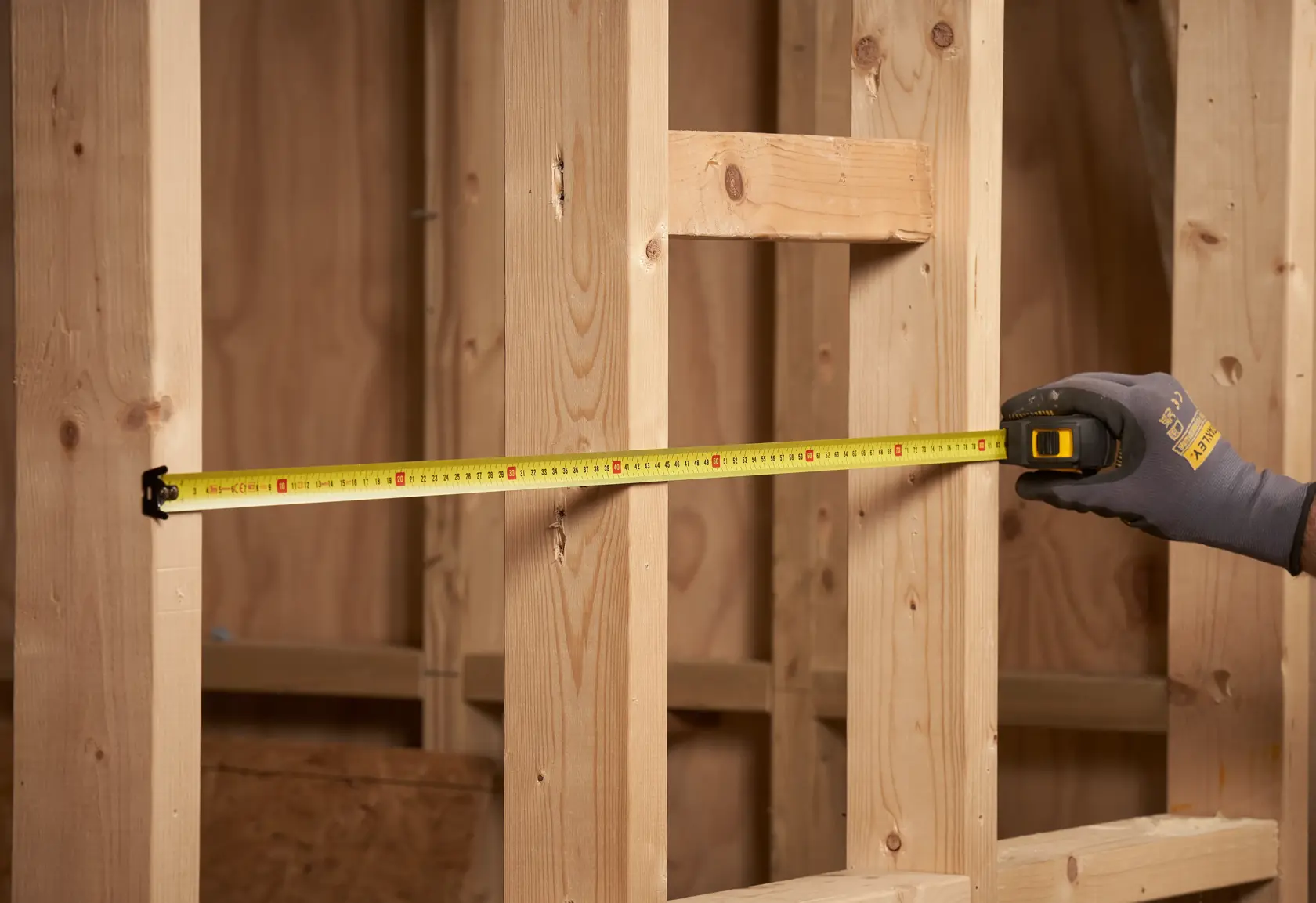 STANLEY STHT0-33559 tape measure measuring wooden framework in construction setting.