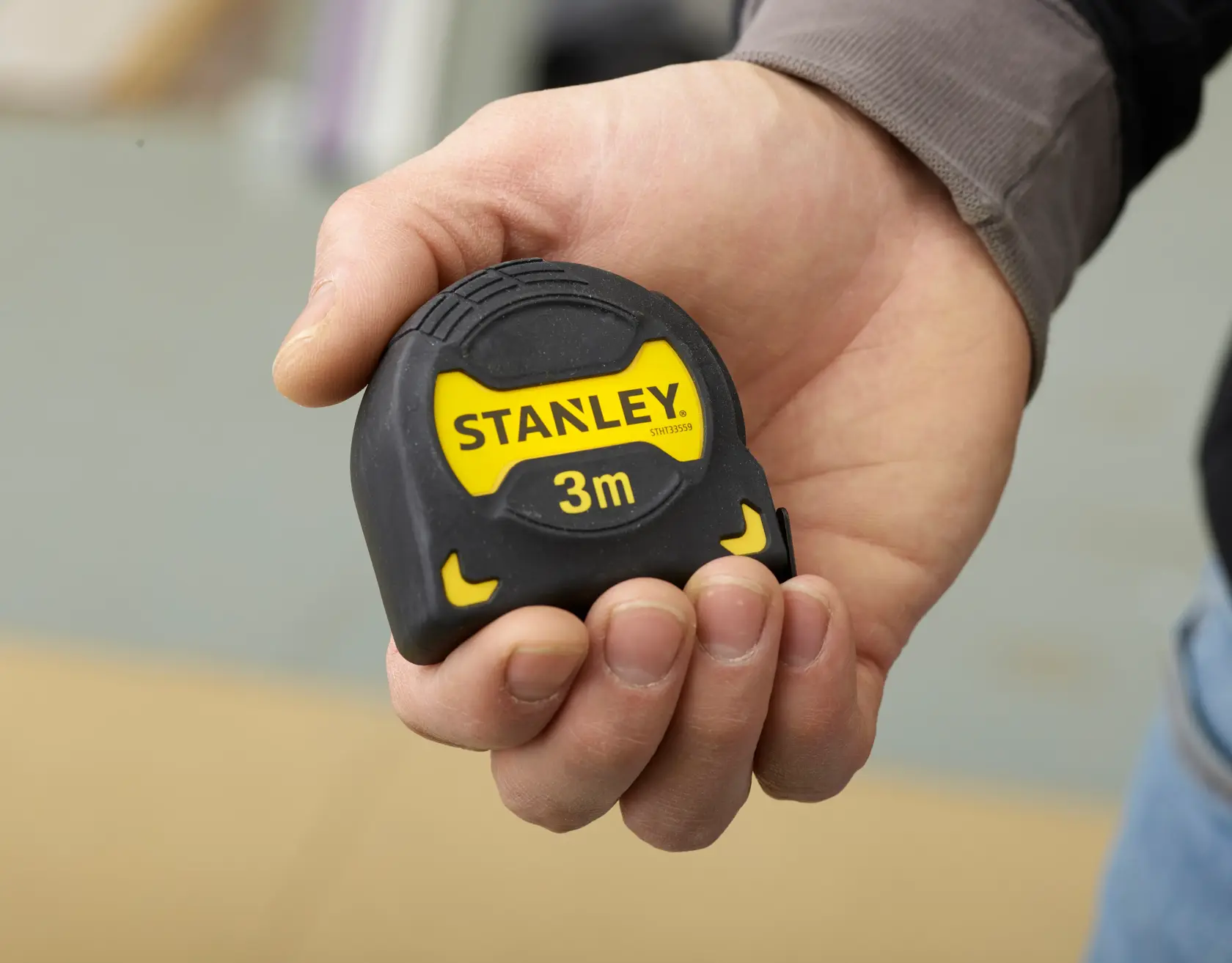 Photo of a hand holding a STANLEY STHT0-33559 3m tape measure, compact design with black and yellow casing.
