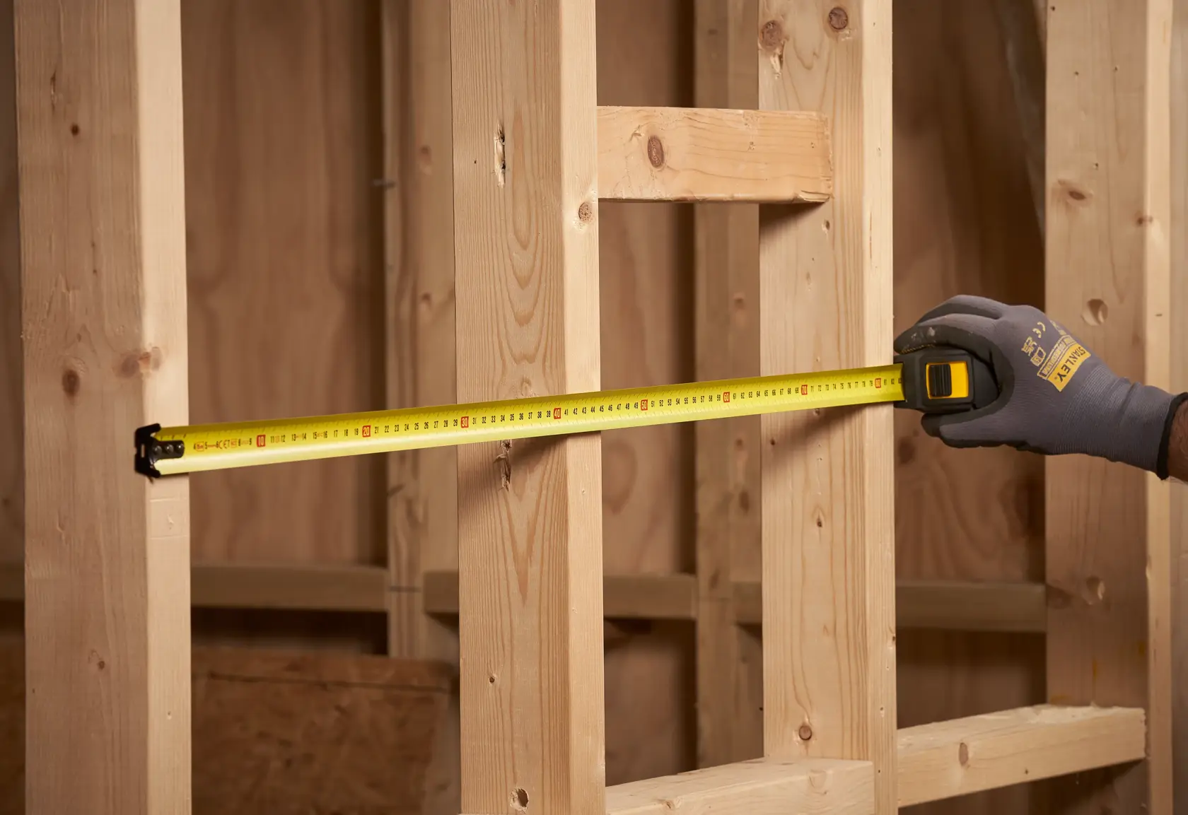 STANLEY STHT0-33561 tape measure in use measuring wooden studs, workshop setting, side view.