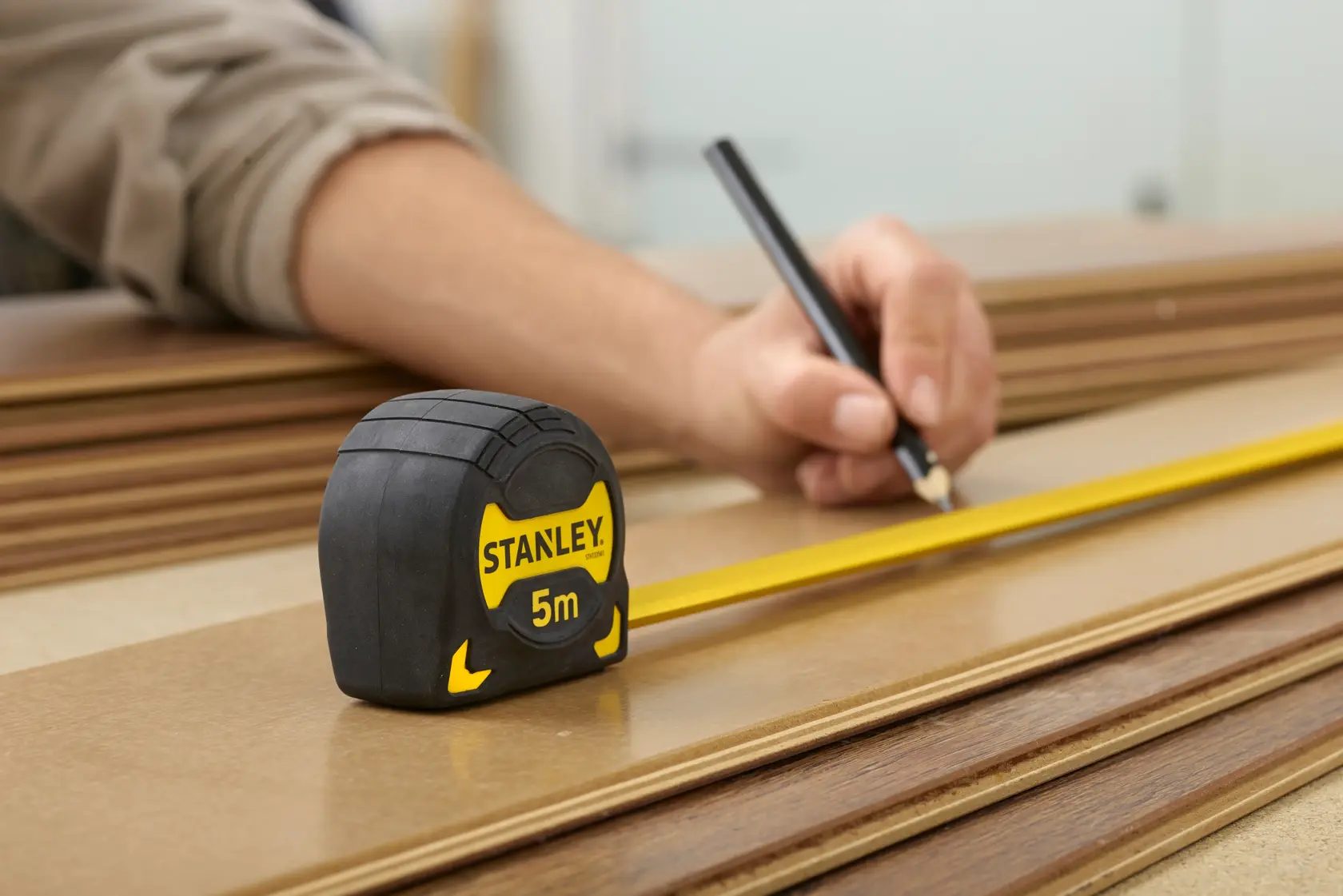 STANLEY STHT0-33561 5m tape measure on wood with a person marking a measurement, close-up photography.