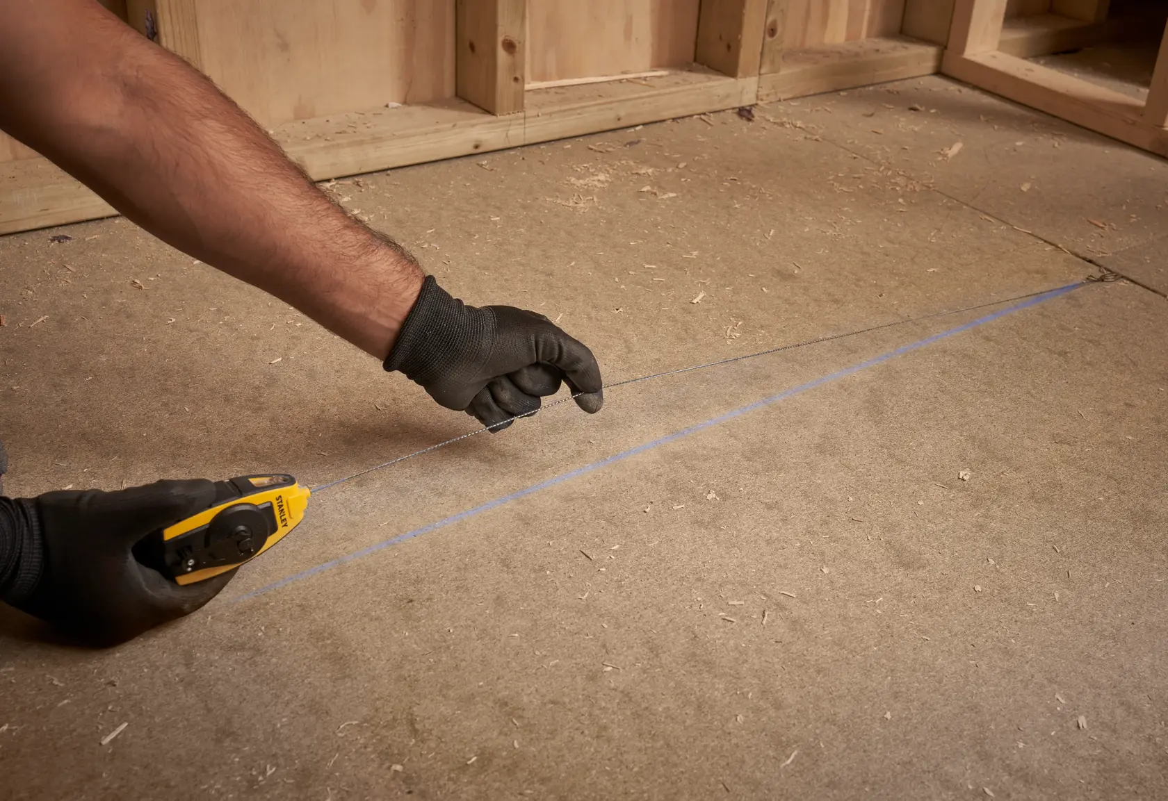 Photo of STANLEY STHT0-47147 chalk line tool in use, marking a straight blue line on a wooden floor.