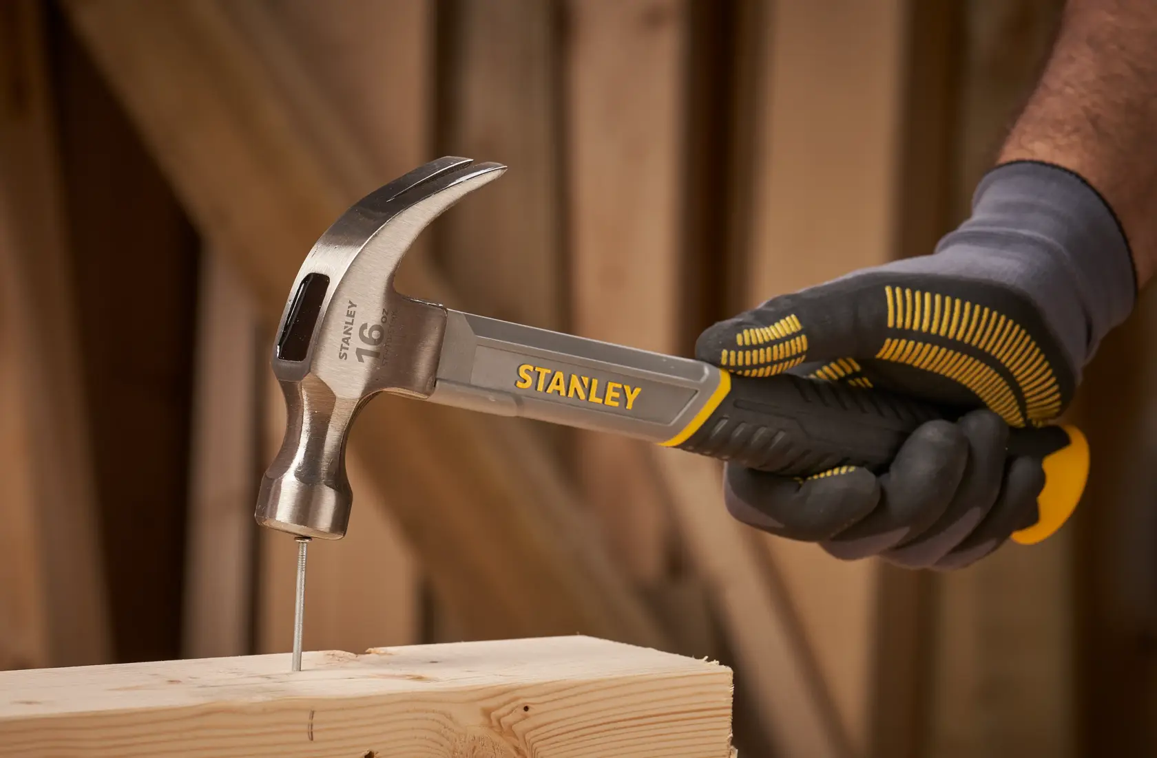 Photo of STANLEY STHT0-51309 claw hammer driving a nail into wood, held in a gloved hand.