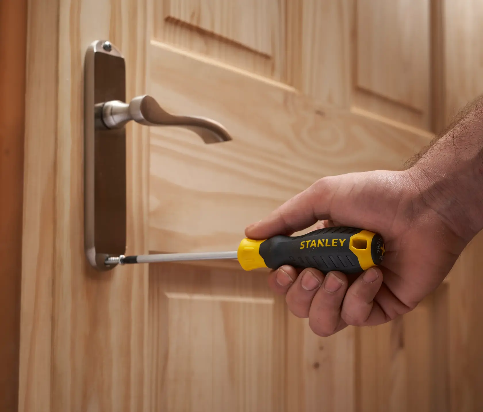 Stanley STHT0-62144 screwdriver used to fasten a screw on a wooden door handle.