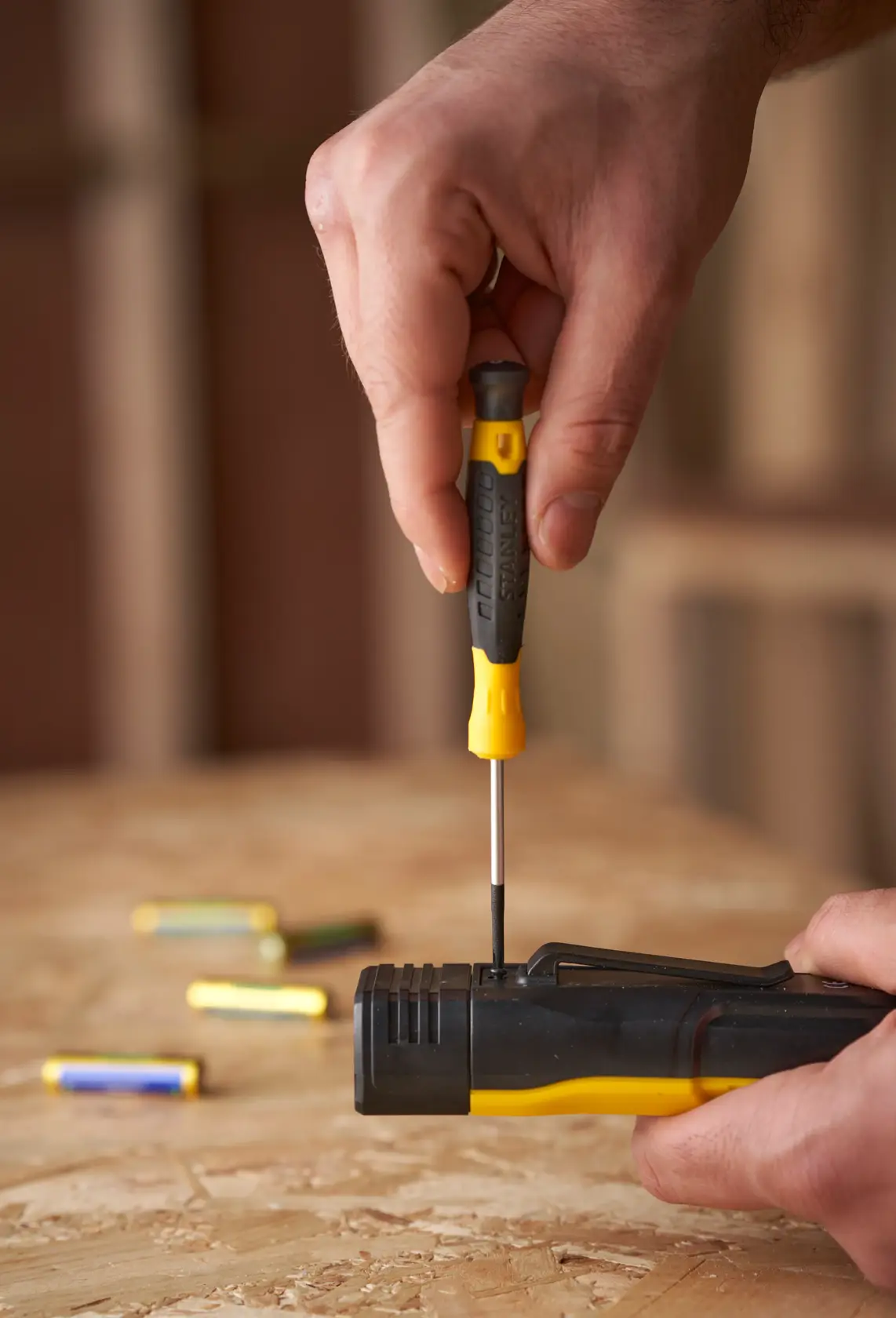 STANLEY STHT0-62144 screwdriver in use on black and yellow device, close-up on wooden surface with batteries.