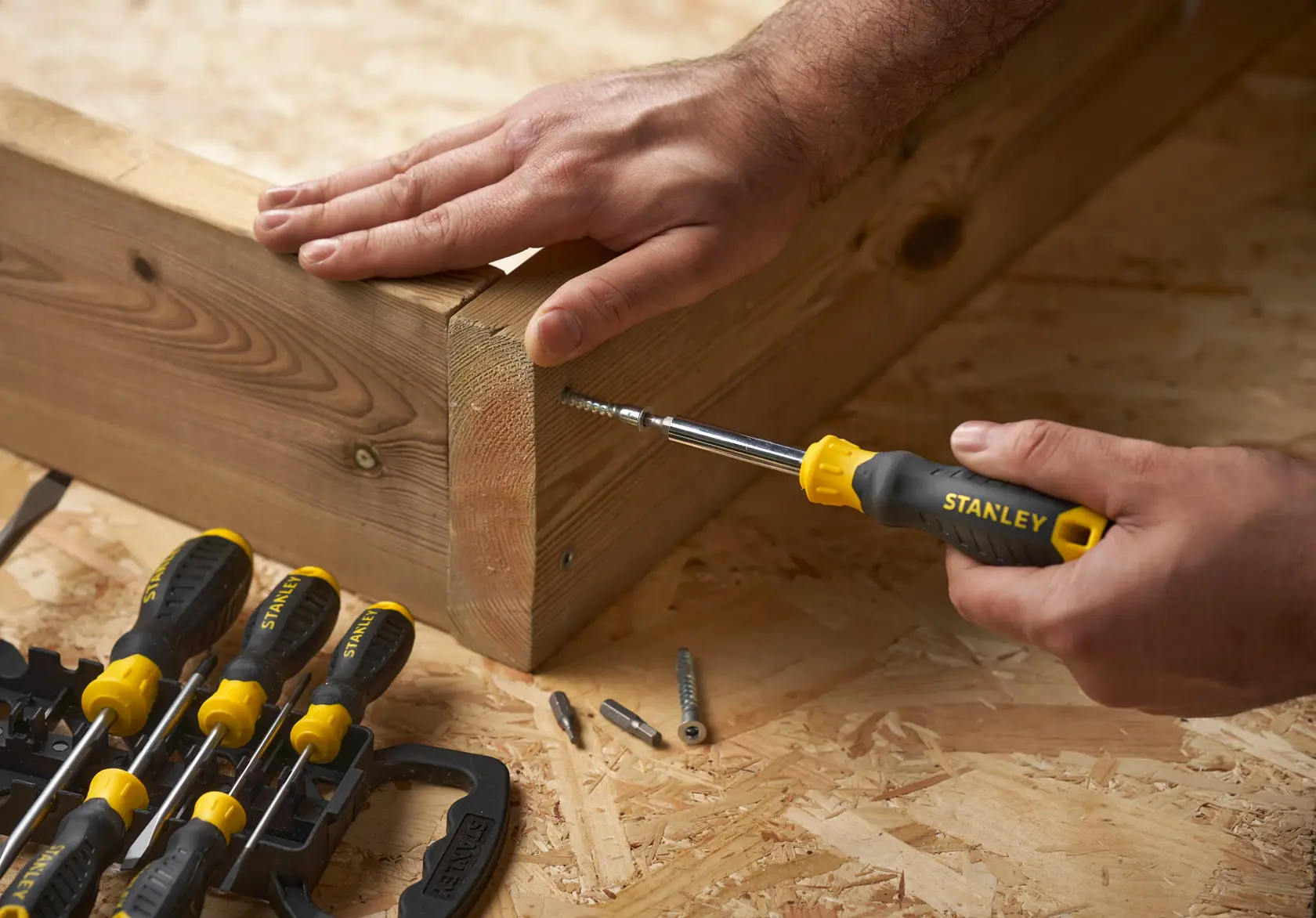 STANLEY STHT0-62144 screwdriver set in use, assembling wooden boards on a workshop table, side angle.
