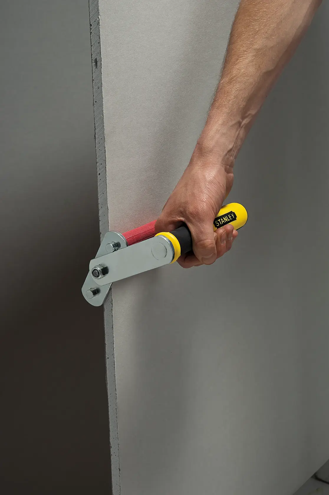 STANLEY STHT1-05868 drywall rasp with yellow handle trimming plasterboard edge, side angle photo.