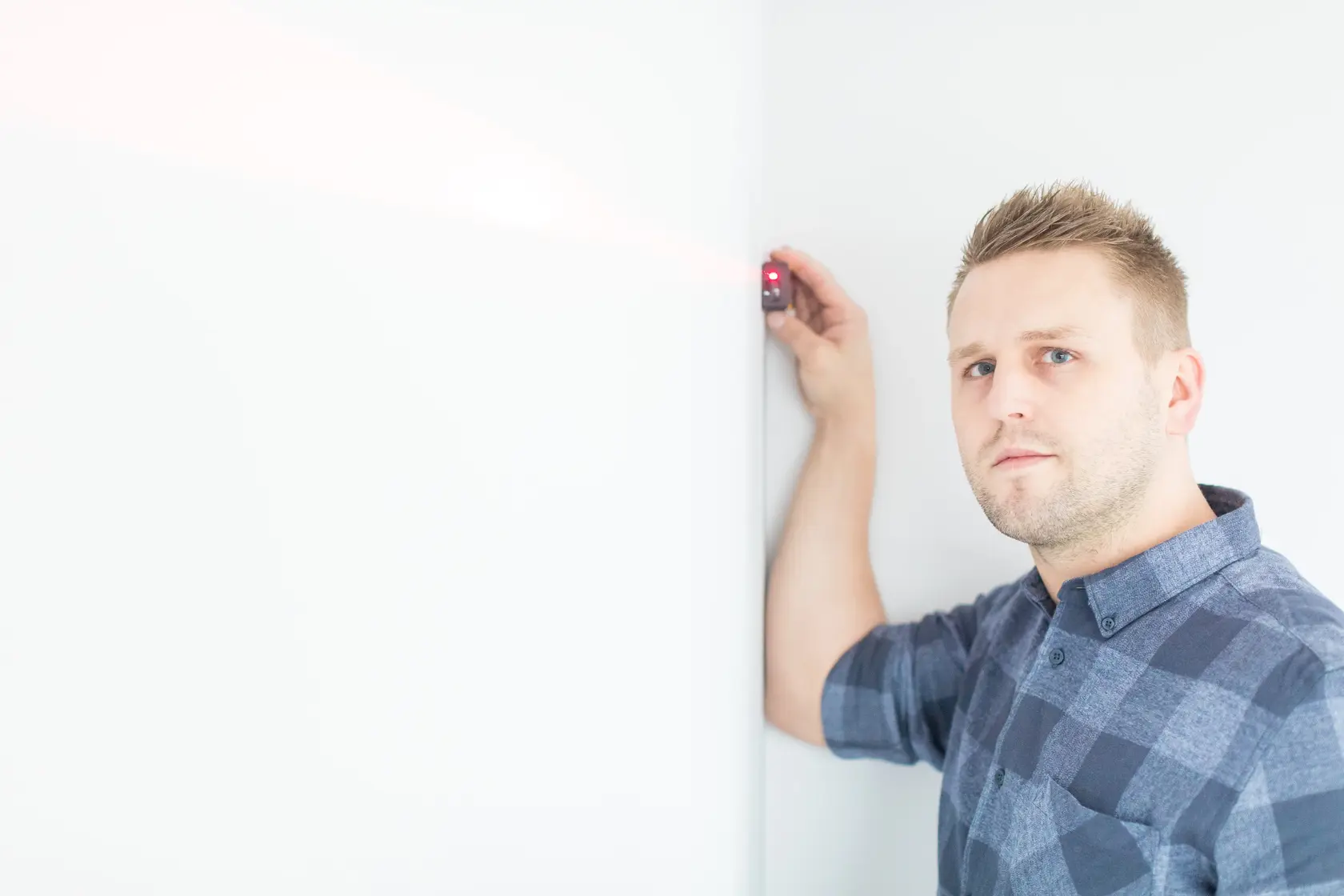 Stanley STHT1-77032 laser distance measurer used against white wall, side angle, man operating.