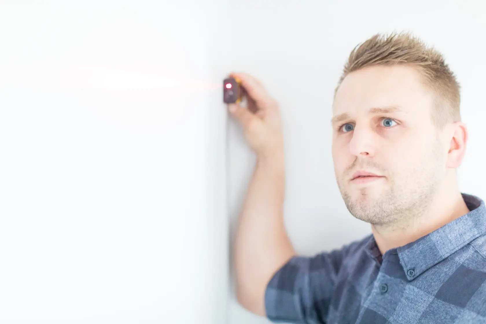 STANLEY STHT1-77032 laser measurer held against a white wall by a person, emitting red laser beam.