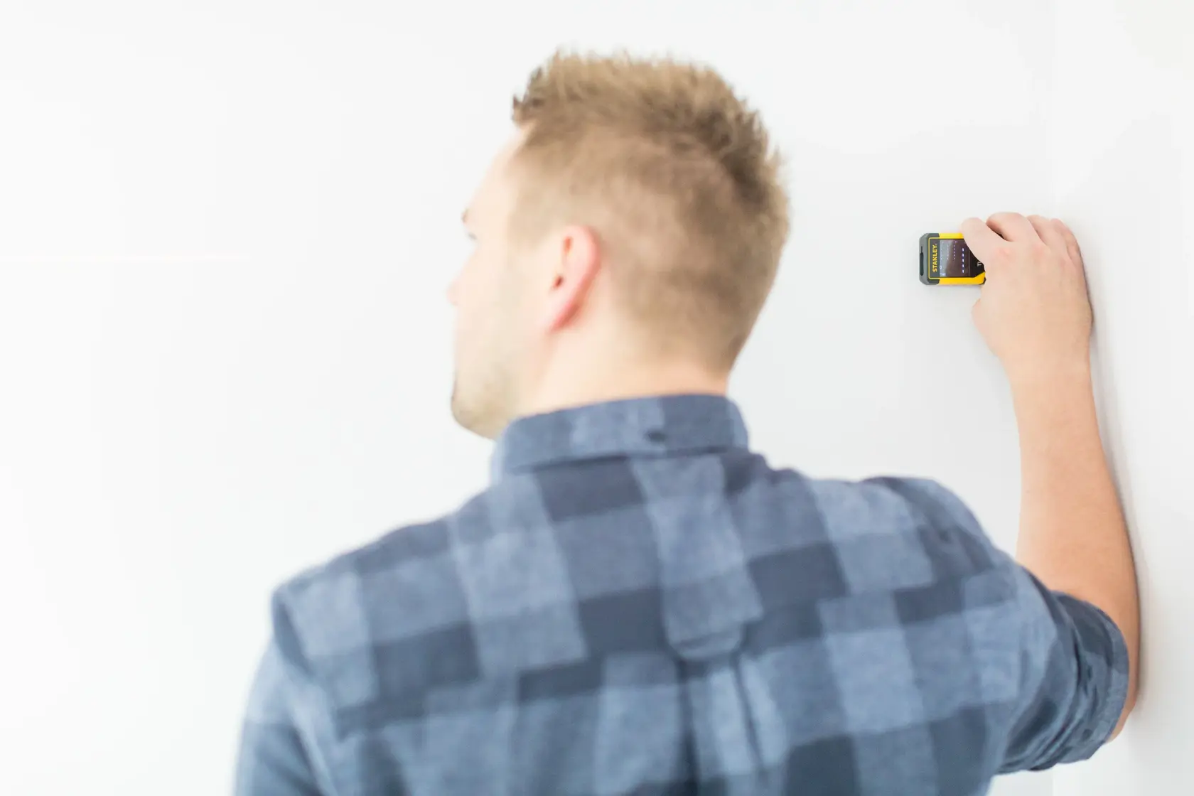Photo of person using STANLEY STHT1-77032 stud finder against white wall, back view.