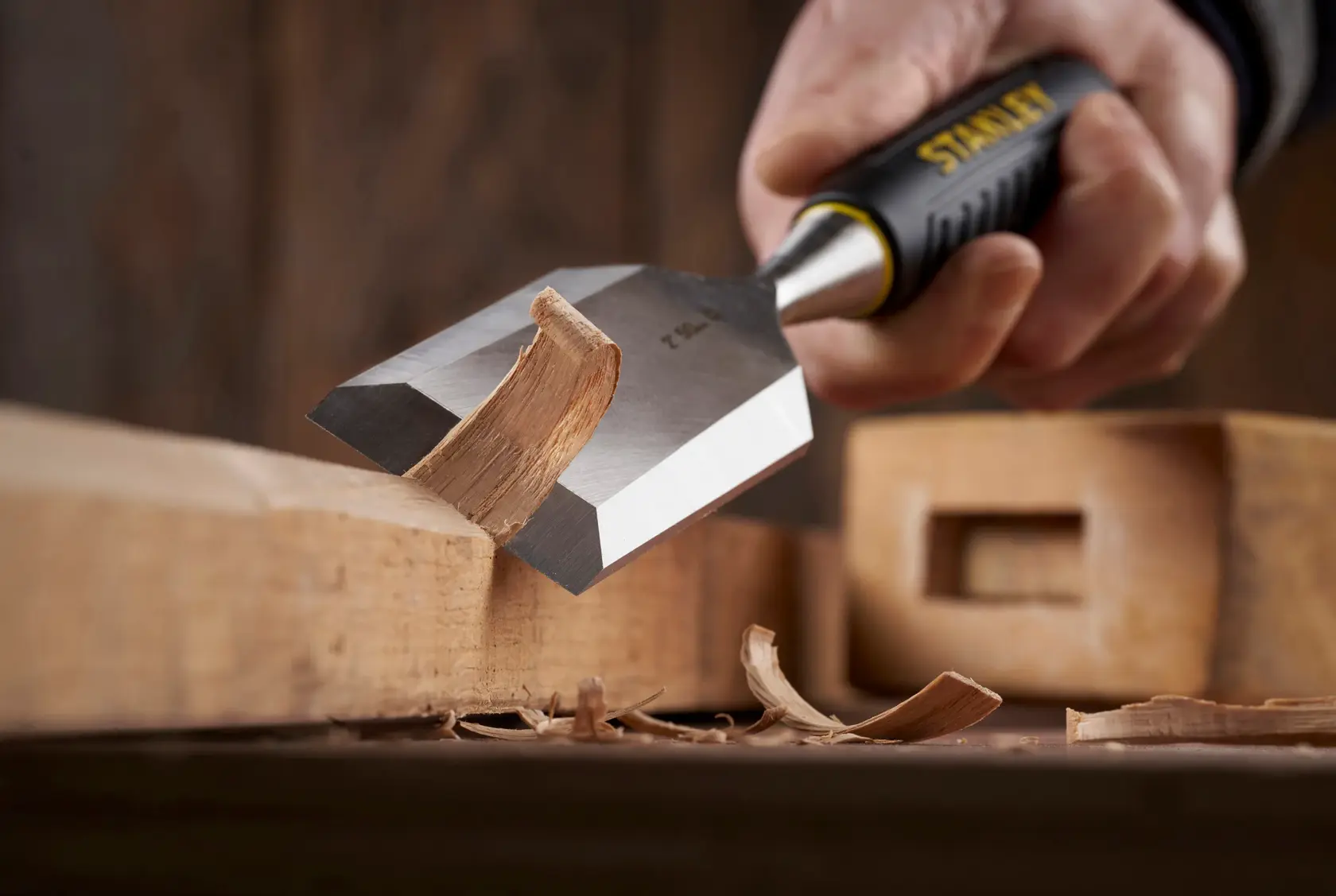 Photo of STANLEY STHT16737-0 chisel with black and yellow handle carving wood, close-up side angle.