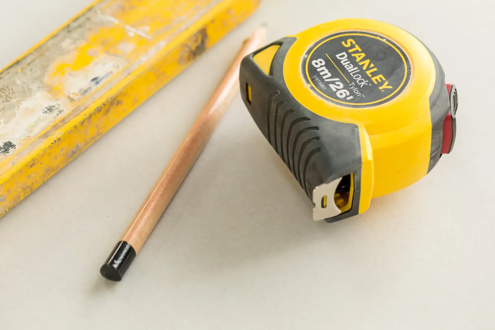 Photo of STANLEY STHT36807-0 tape measure with black-yellow case, pencil, and yellow ruler on a light surface.