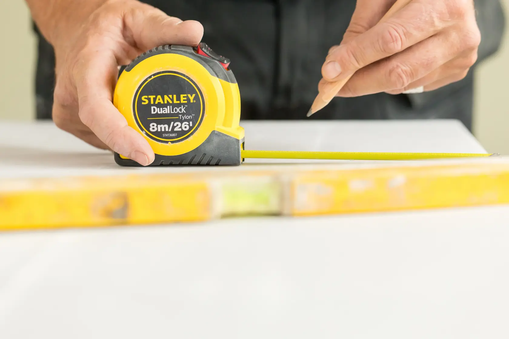 STANLEY STHT36807-0 tape measure held by hand, yellow casing, DualLock, used for marking measurements.