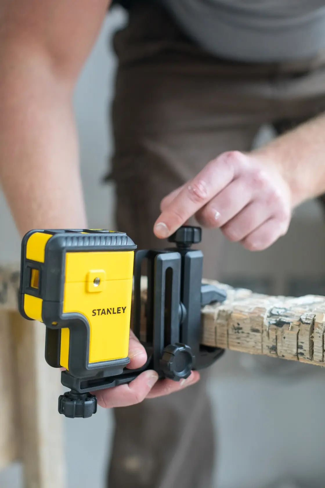 STANLEY STHT77503-1 laser level attached to a wooden beam, user adjusting mounting bracket.