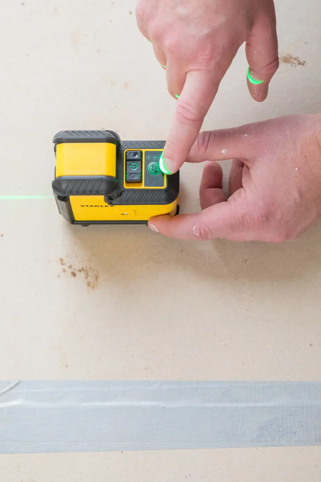 STANLEY STHT77594-1 laser level being operated, close-up of hand pressing power button, green laser line visible.