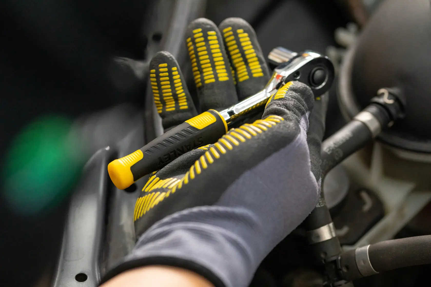 STANLEY STMT82831-1 ratchet wrench held by gloved hand, black and yellow handle, automotive context.
