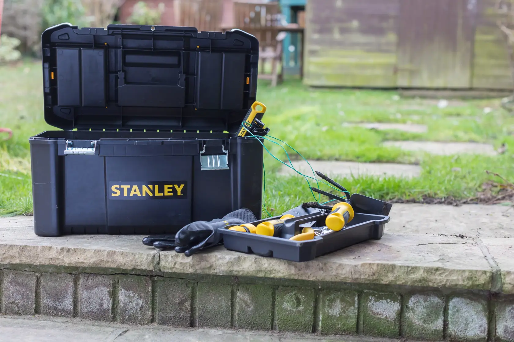 STANLEY STST1-75521 black toolbox open outdoors with yellow-handled tools and gloves on a stone step.