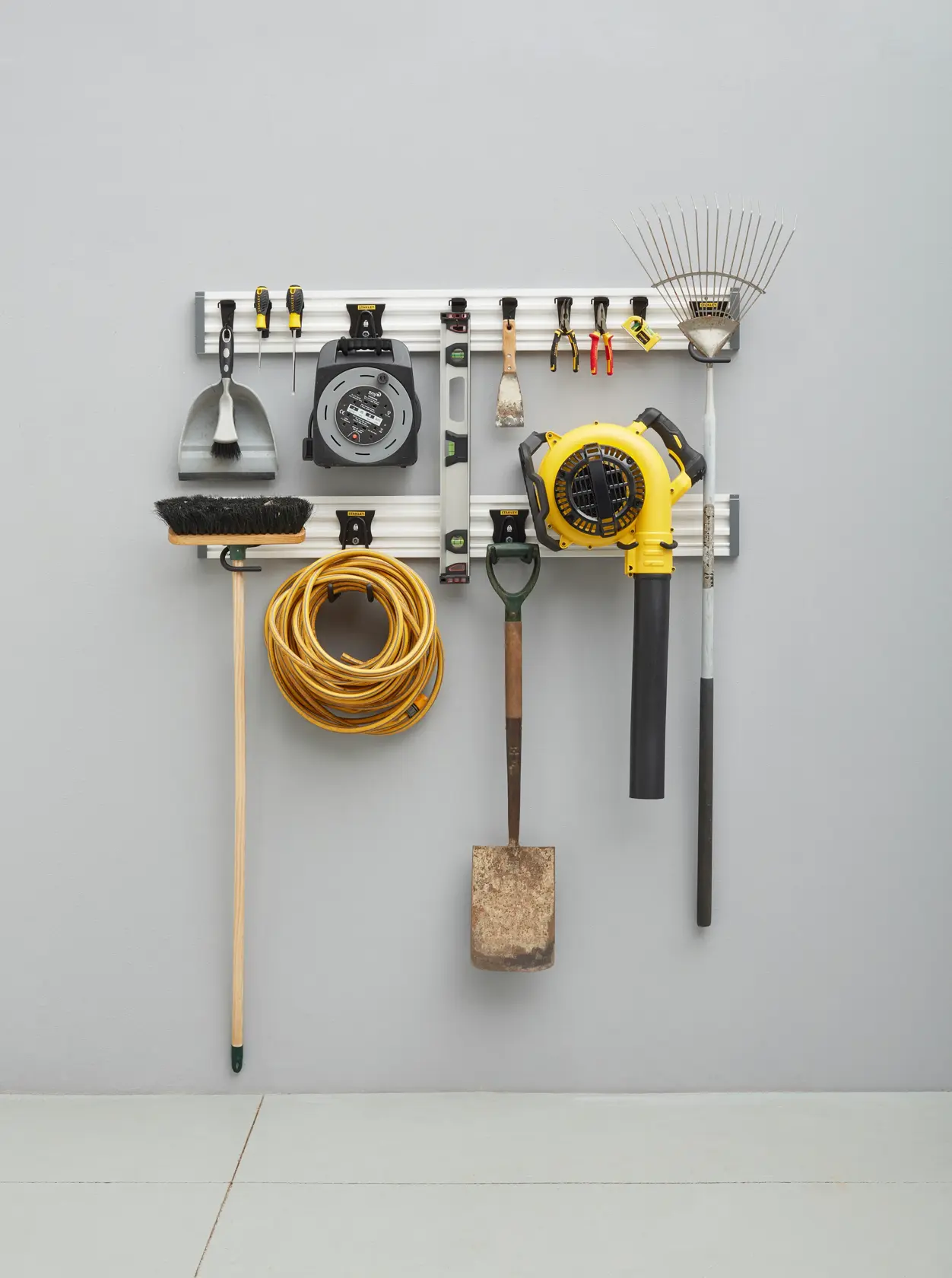 STANLEY STST22000-1 wall-mounted organizer rail holding various tools including rake, blower, broom, cord, and hand tools.