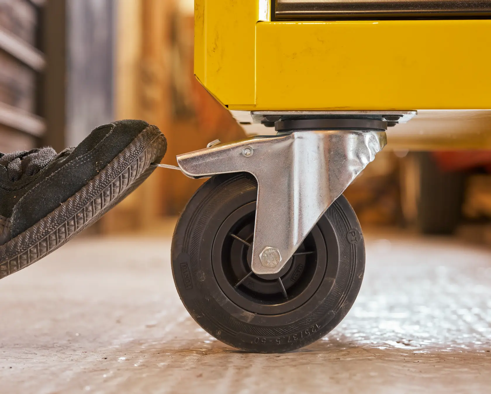 STANLEY STST74306-1 photography of yellow tool chest caster wheel with foot pressing brake lever, side angle.
