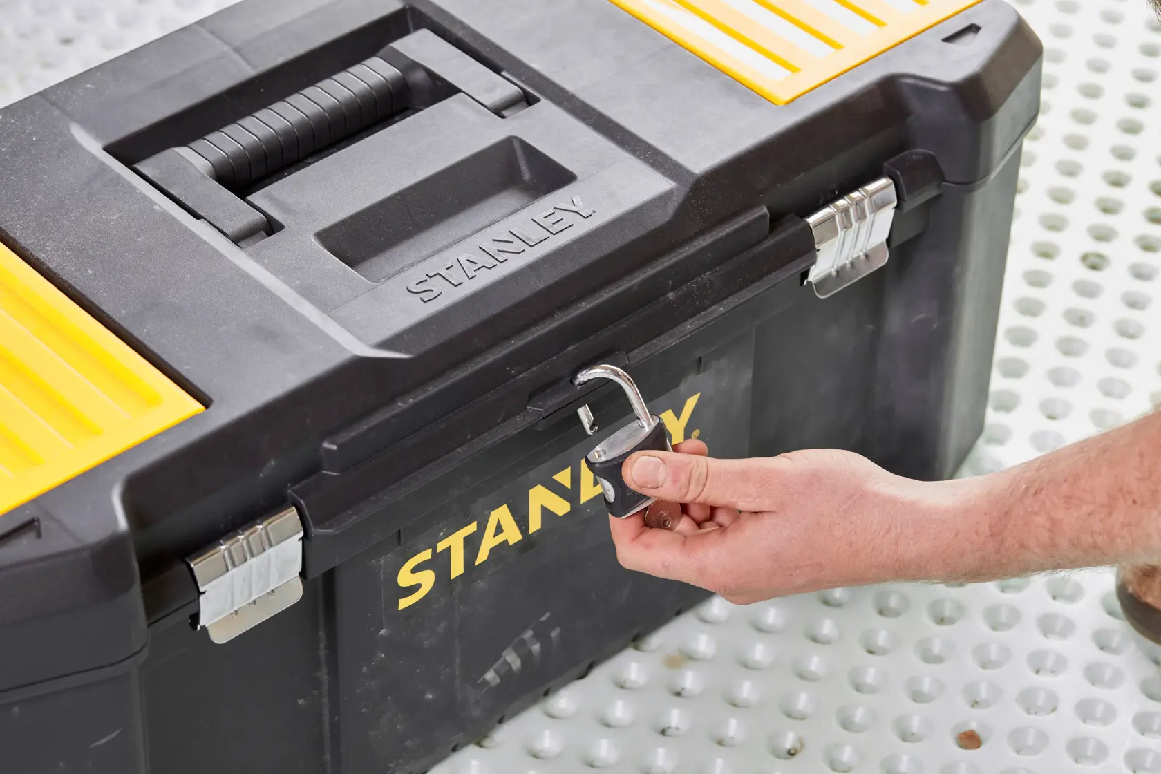 STANLEY STST82976-1 toolbox front angle, black and yellow with padlock being unlocked by hand.