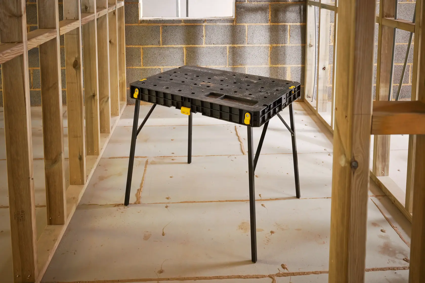 STANLEY STST83492-1 workbench table, black plastic top with foldable legs, shown in construction setting.