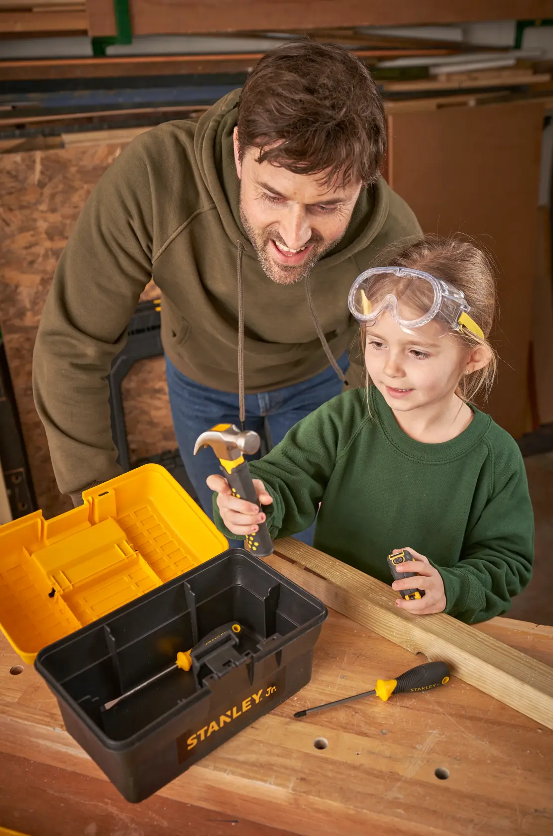 Photo of STANLEY TBS001-05-SY kids tool set on workbench, toolbox open, child using hammer, adult supervising.