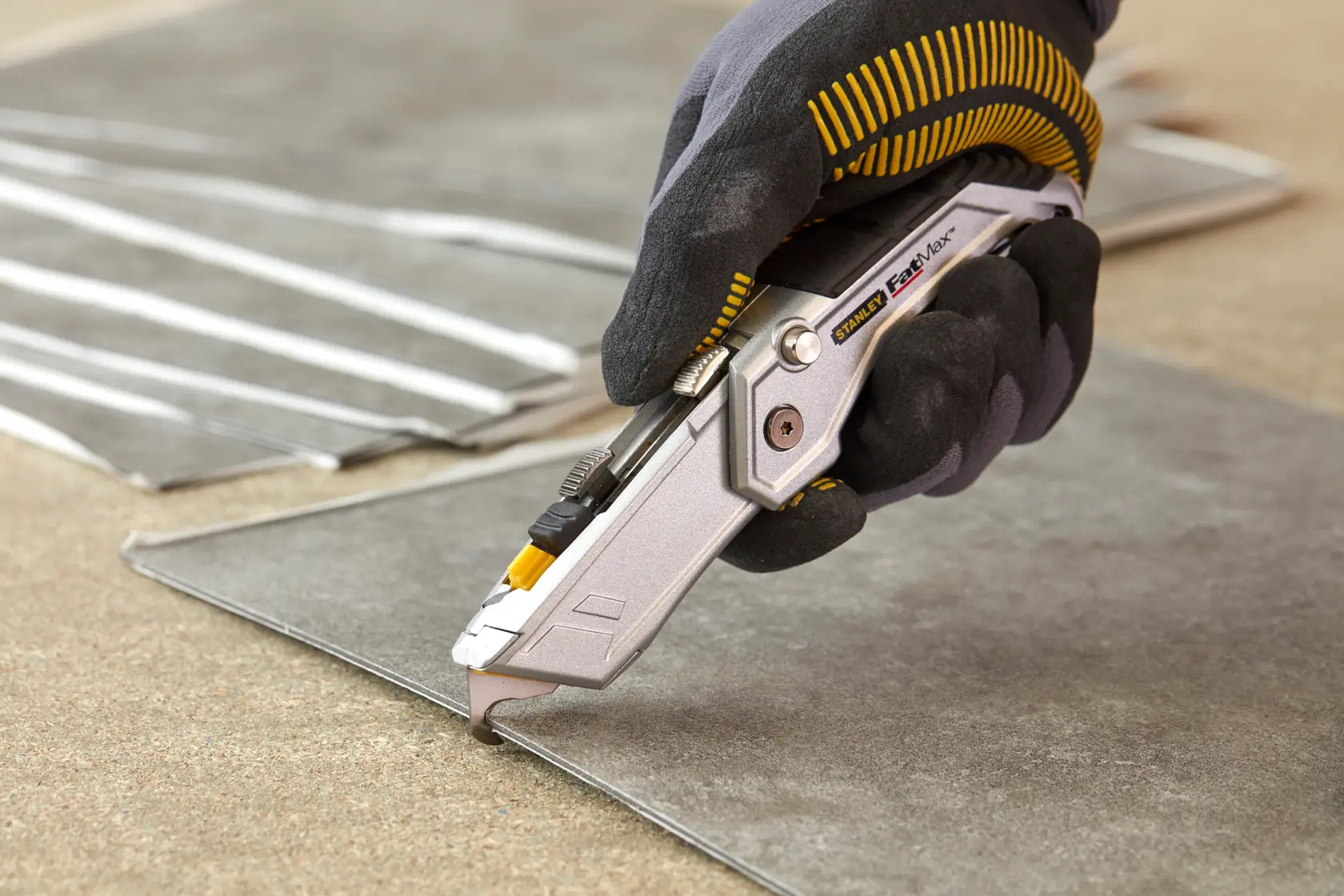 STANLEY XTHT0-10502 utility knife cutting tile, close-up photo, worker wearing black glove.
